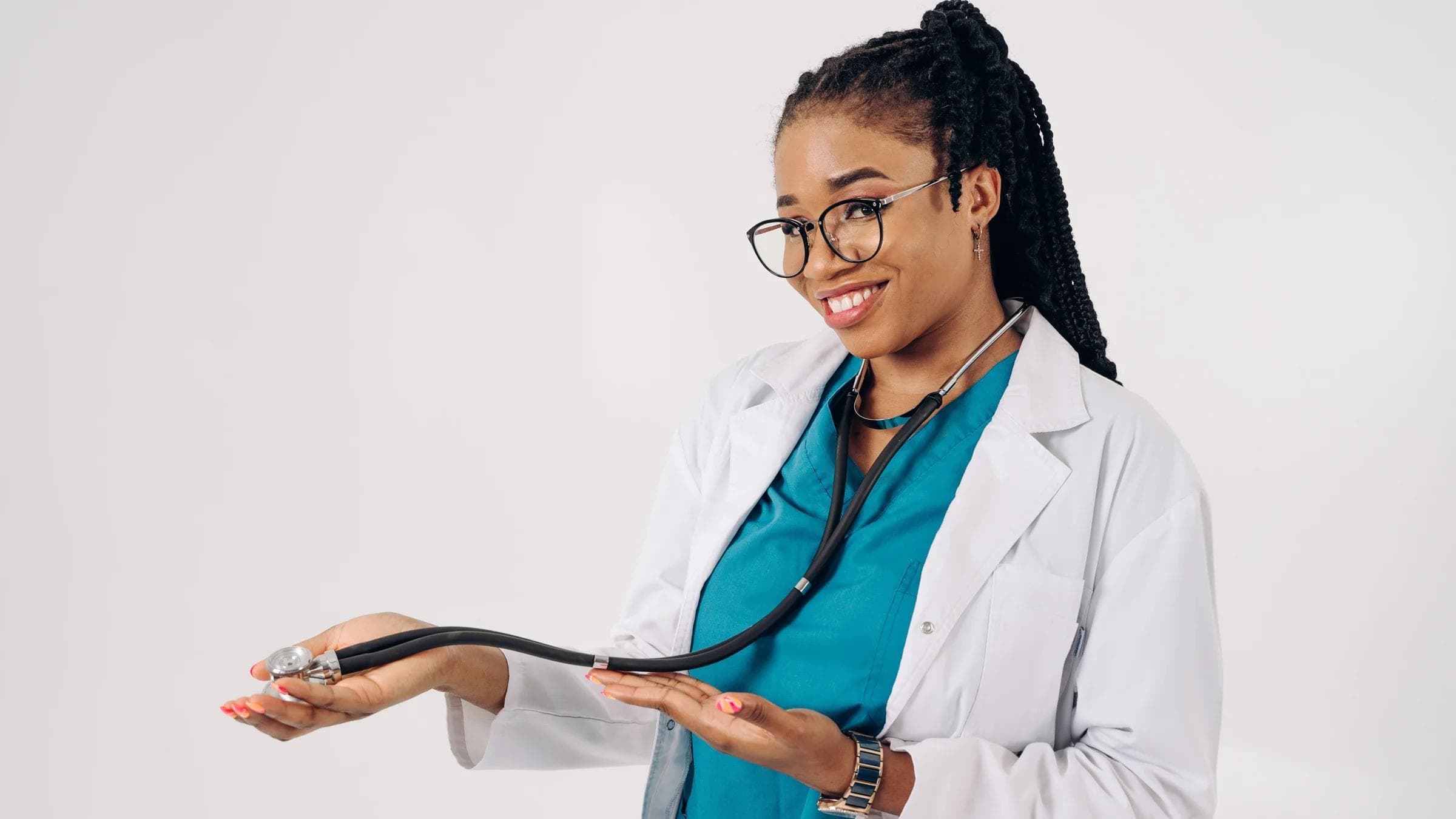 Smiling female doctor holding a stethoscope, wearing glasses and scrubs on a white background.