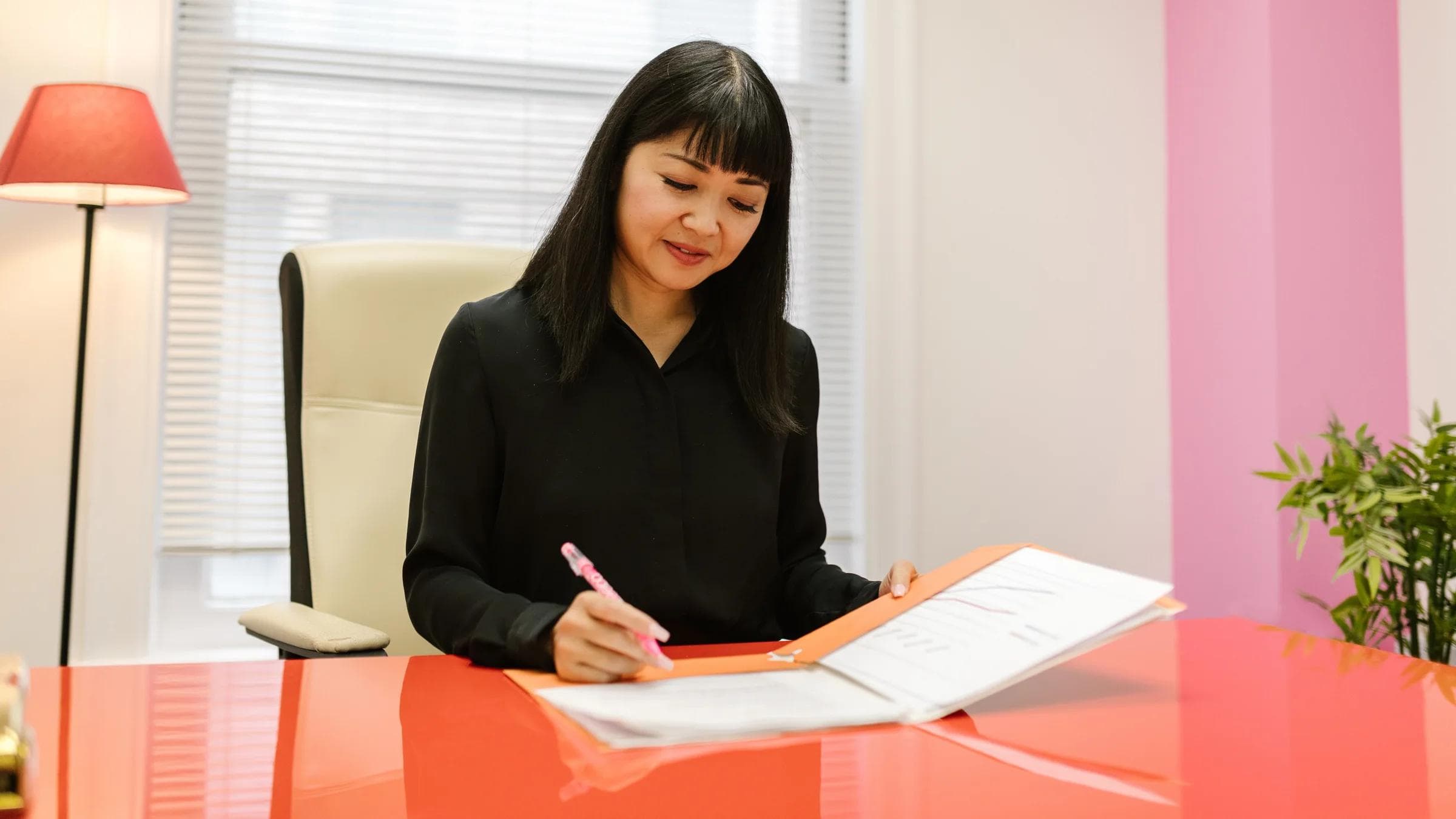 Asian woman working in a bright modern indoor office setting reviewing paperwork.