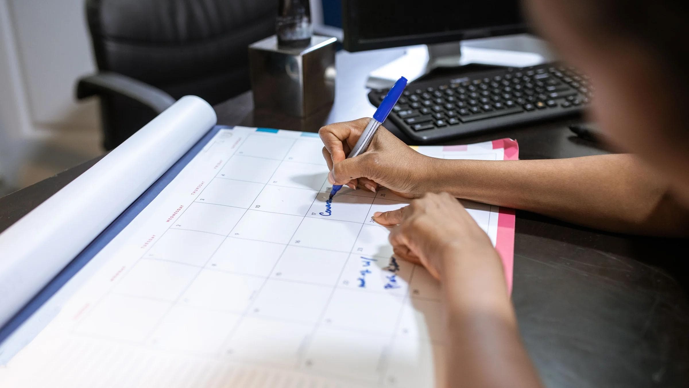 Close-up of a woman planning her schedule on a desk calendar in an office setting.