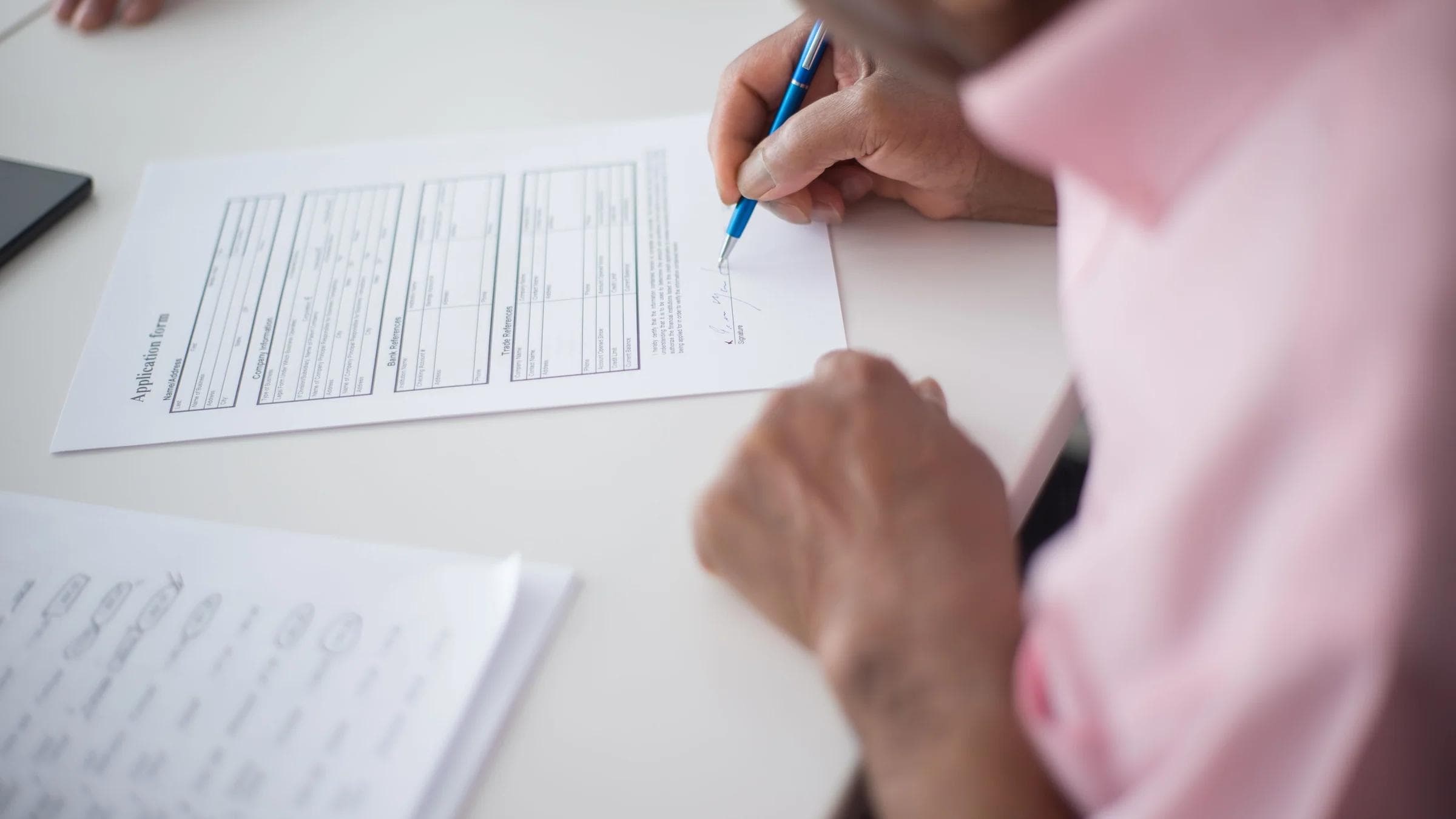 Elderly man signing important business document at desk in office setting.