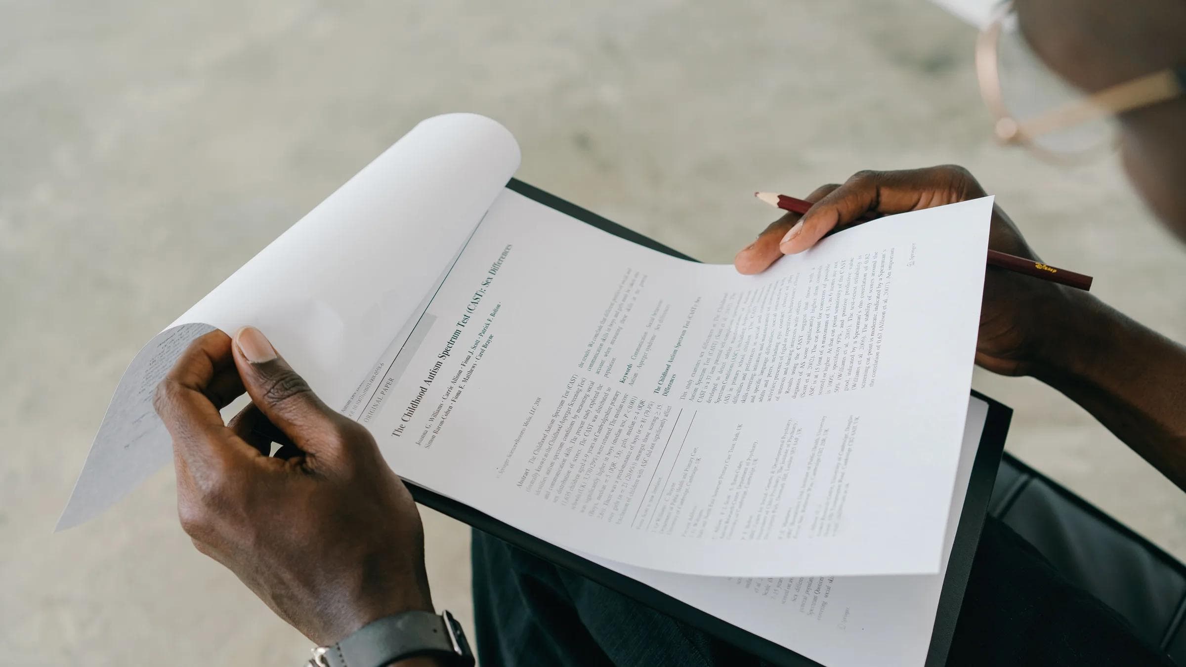 Hands holding and reviewing business documents with a pen, focusing on detailed paperwork.