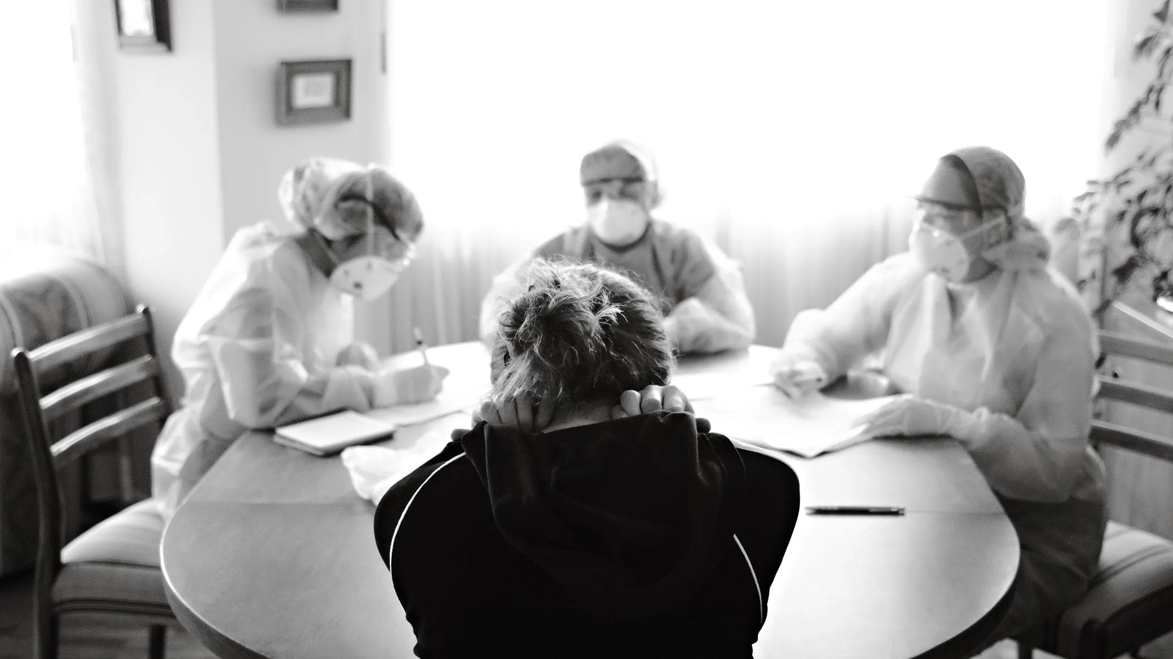 Healthcare team in protective equipment engaging with a person at a table, highlighting medical discussion in pandemic setting.