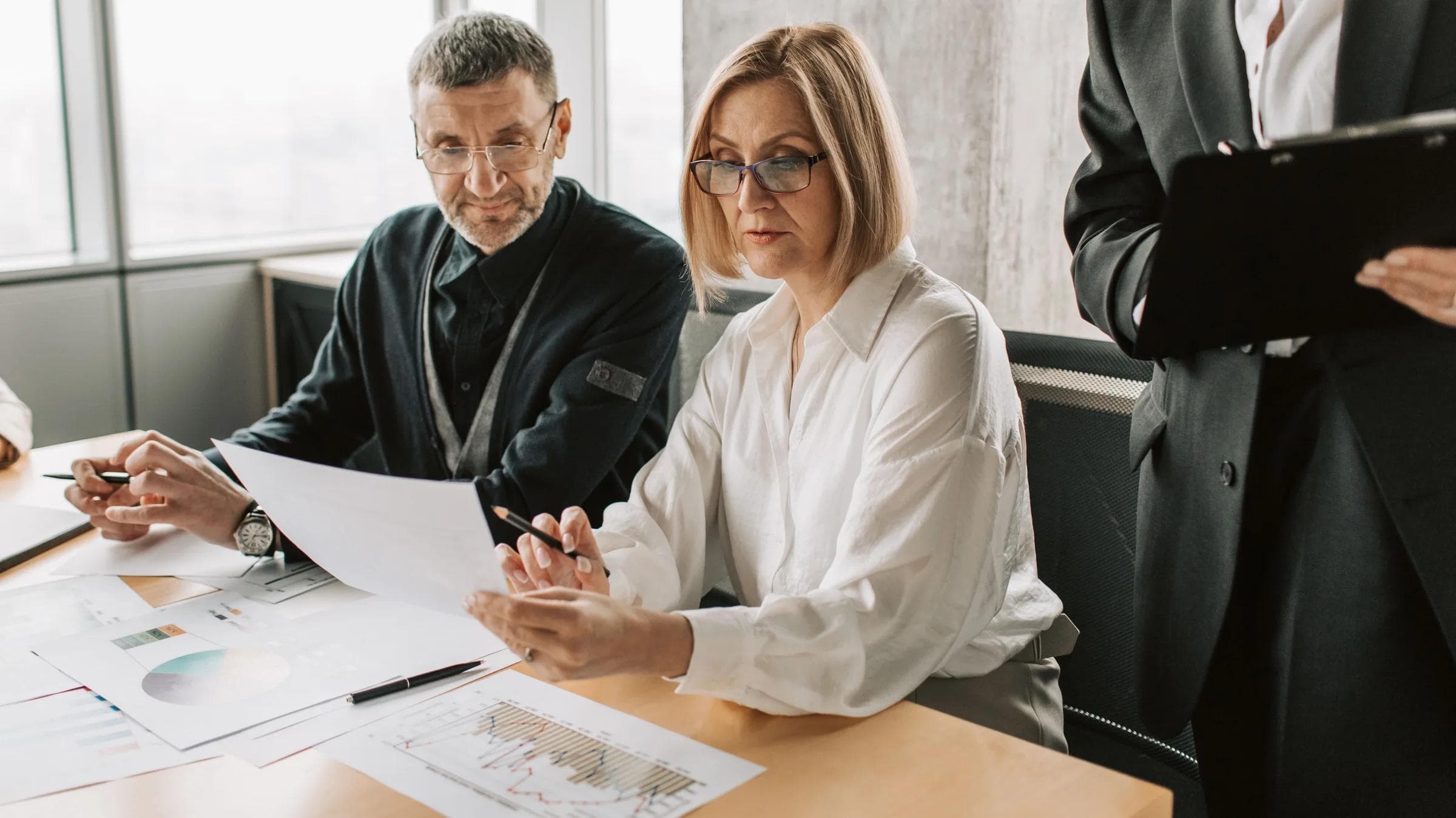 Business professionals engaged in a meeting, analyzing documents and charts in a modern office.