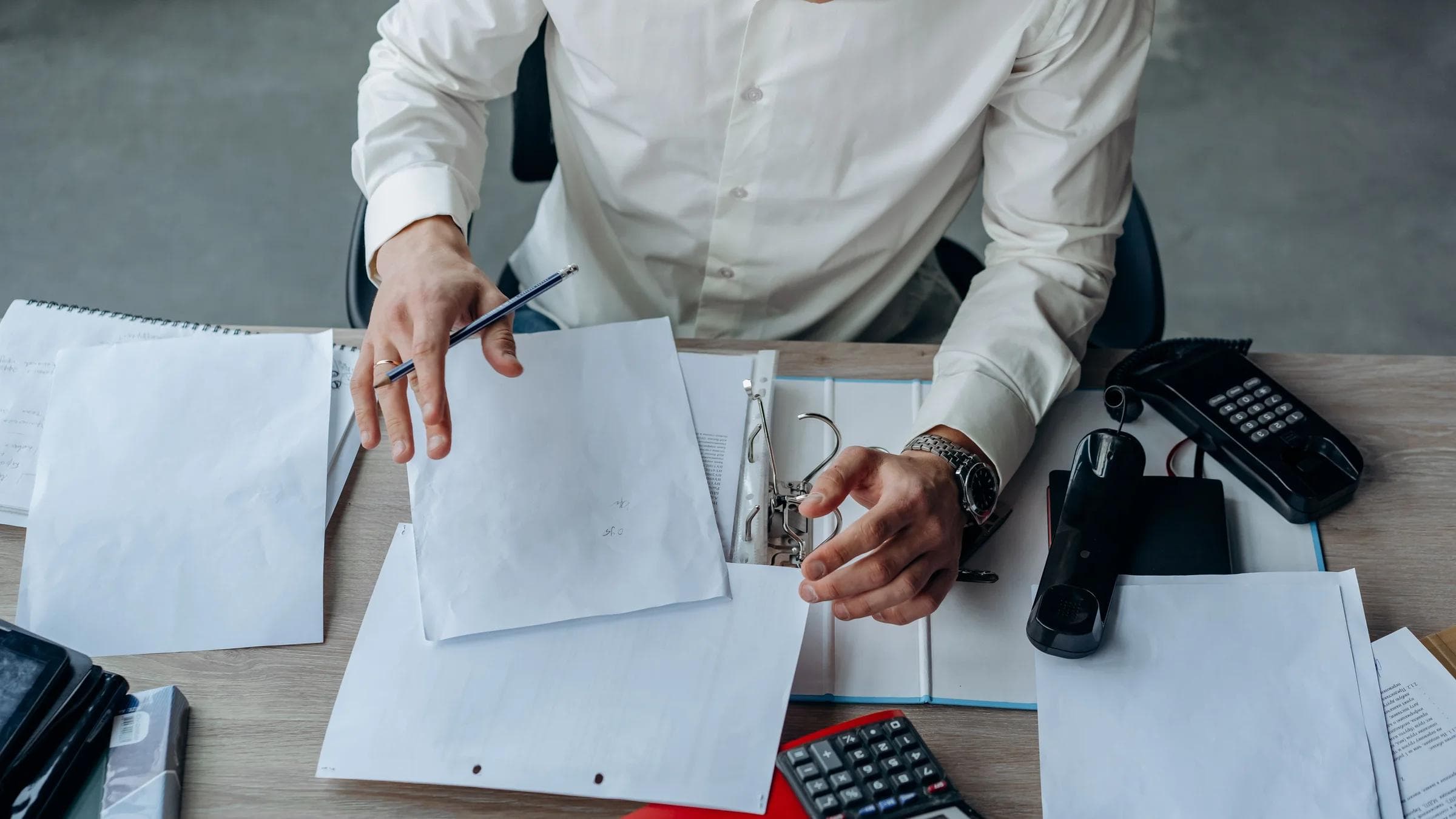 A business professional organizing documents at a busy office desk, emphasizing productivity.