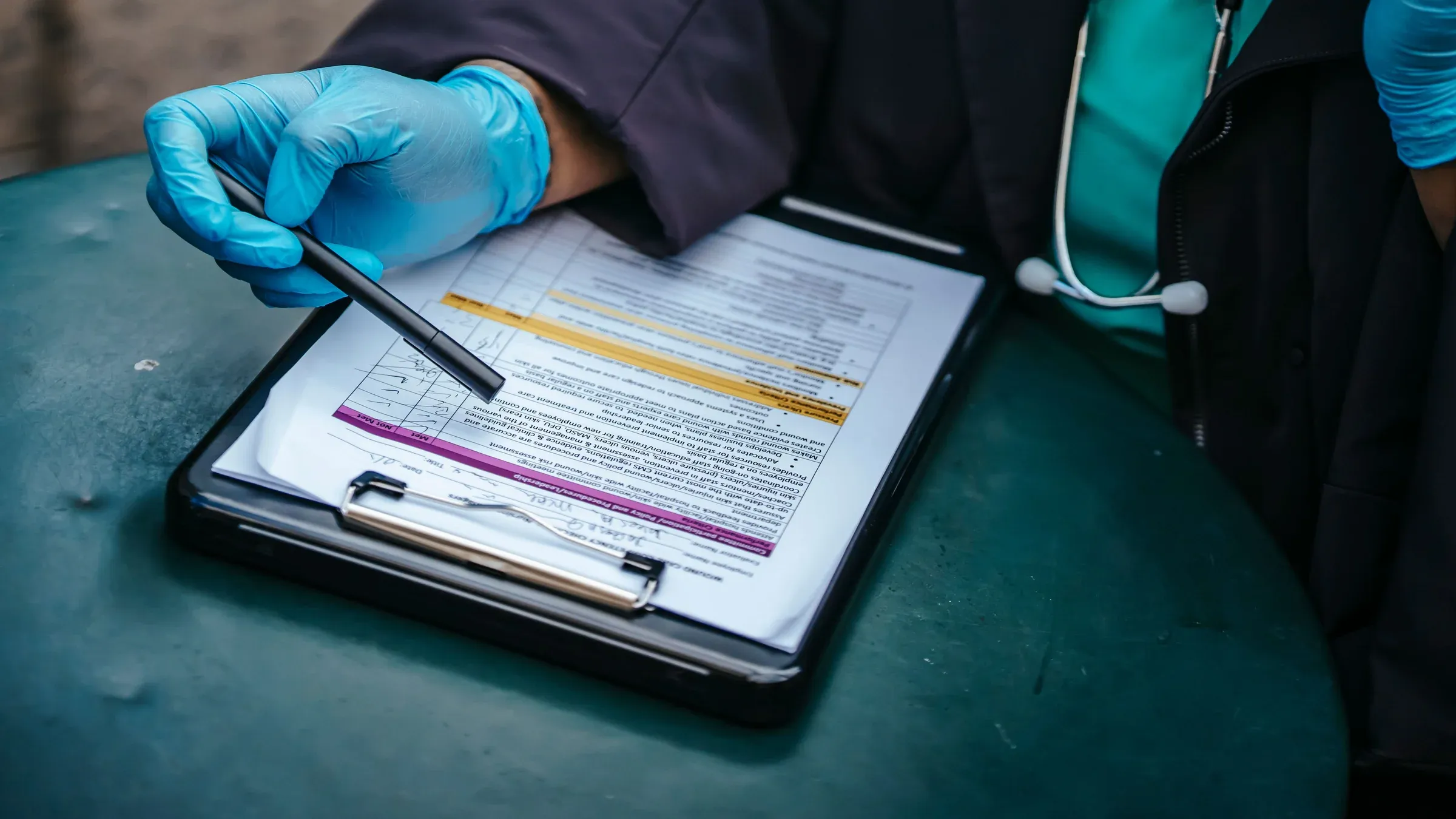 From above of crop anonymous plump female doctor in disposable gloves working at table with paper on clipboard.