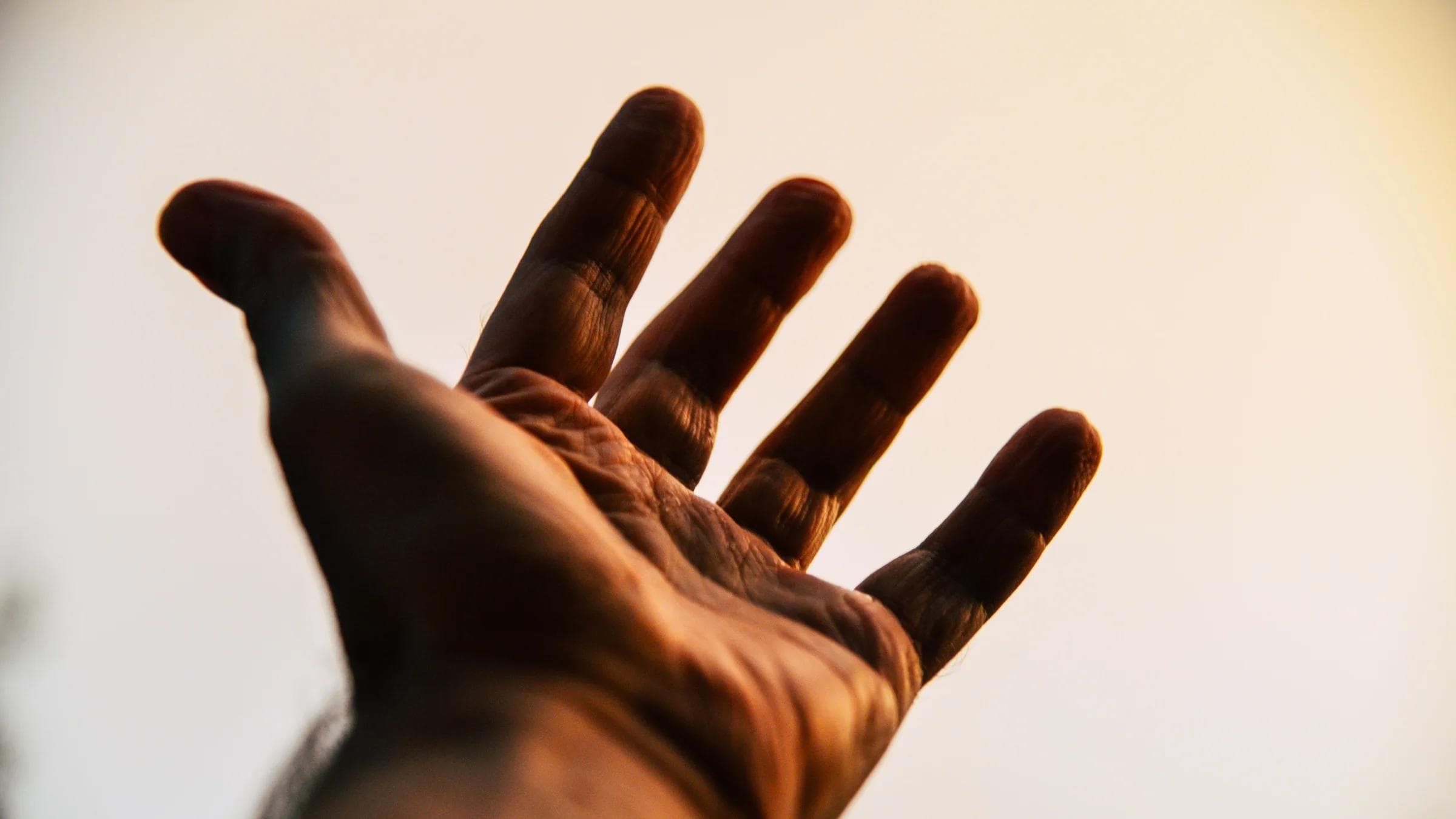 A human hand reaching toward the sky, silhouetted against a bright, warm backdrop.