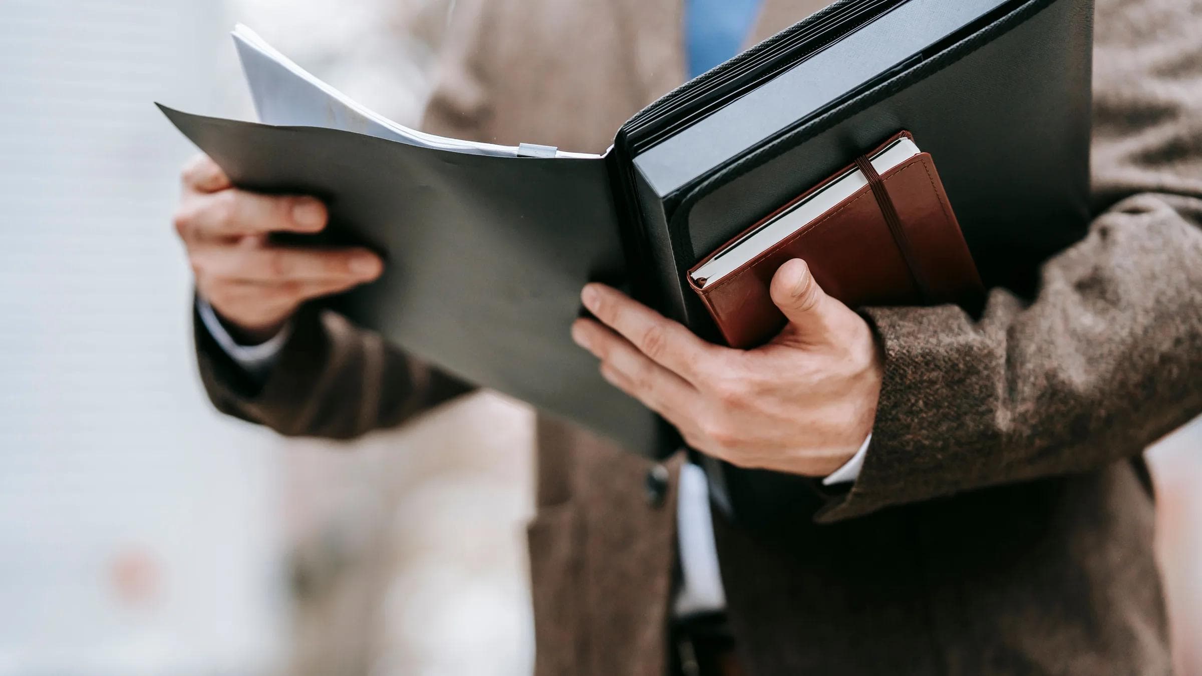 A professional in formal attire holding a notepad and folder outside, emphasizing business and focus.