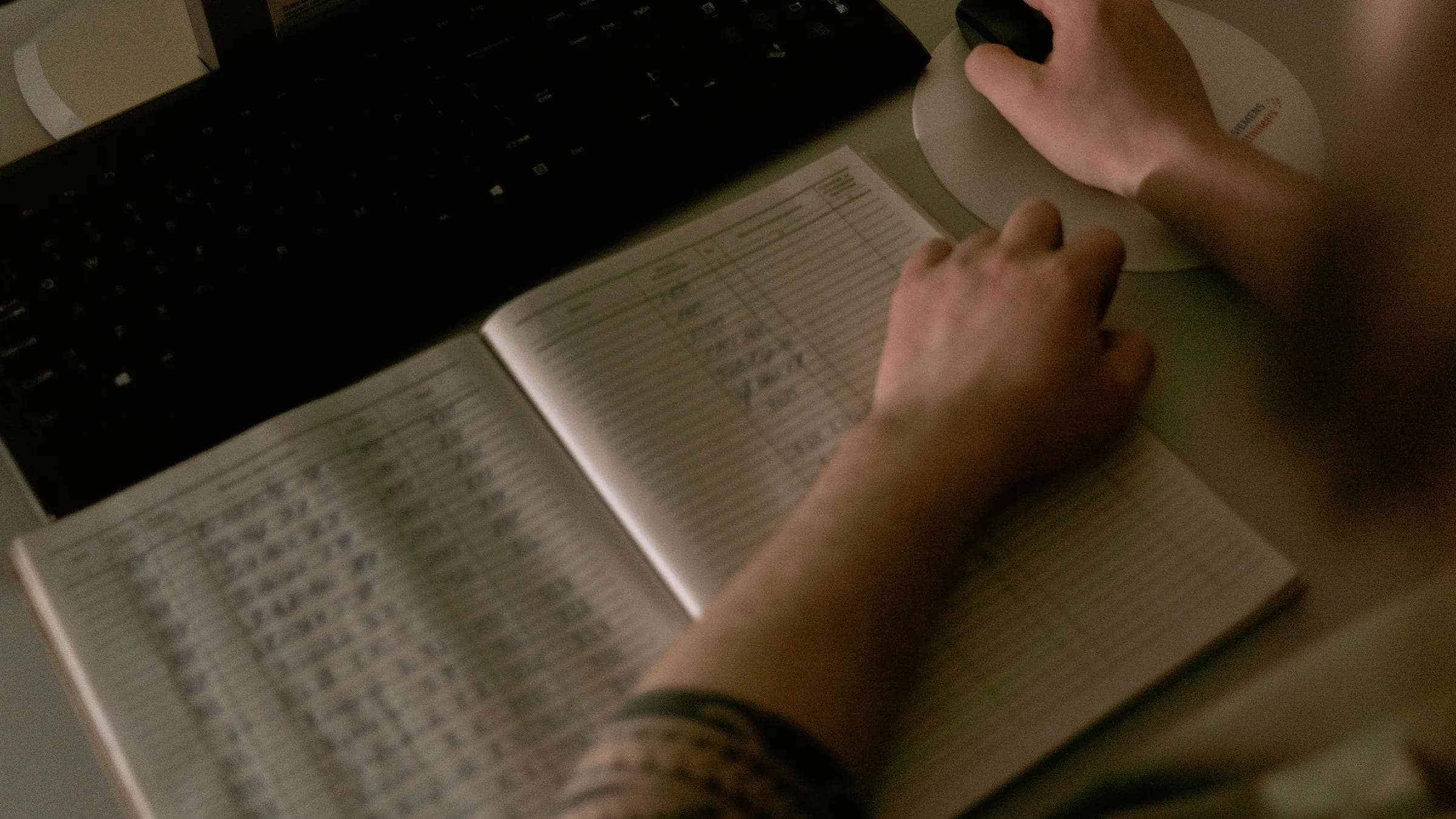 A healthcare worker reviews medical records on a computer beside handwritten notes.