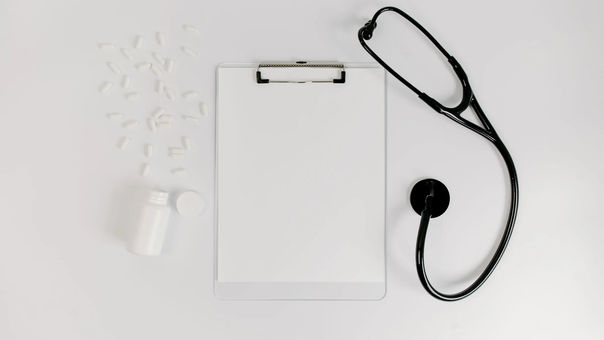 Flat lay of clipboard, pills, and stethoscope for medical use.