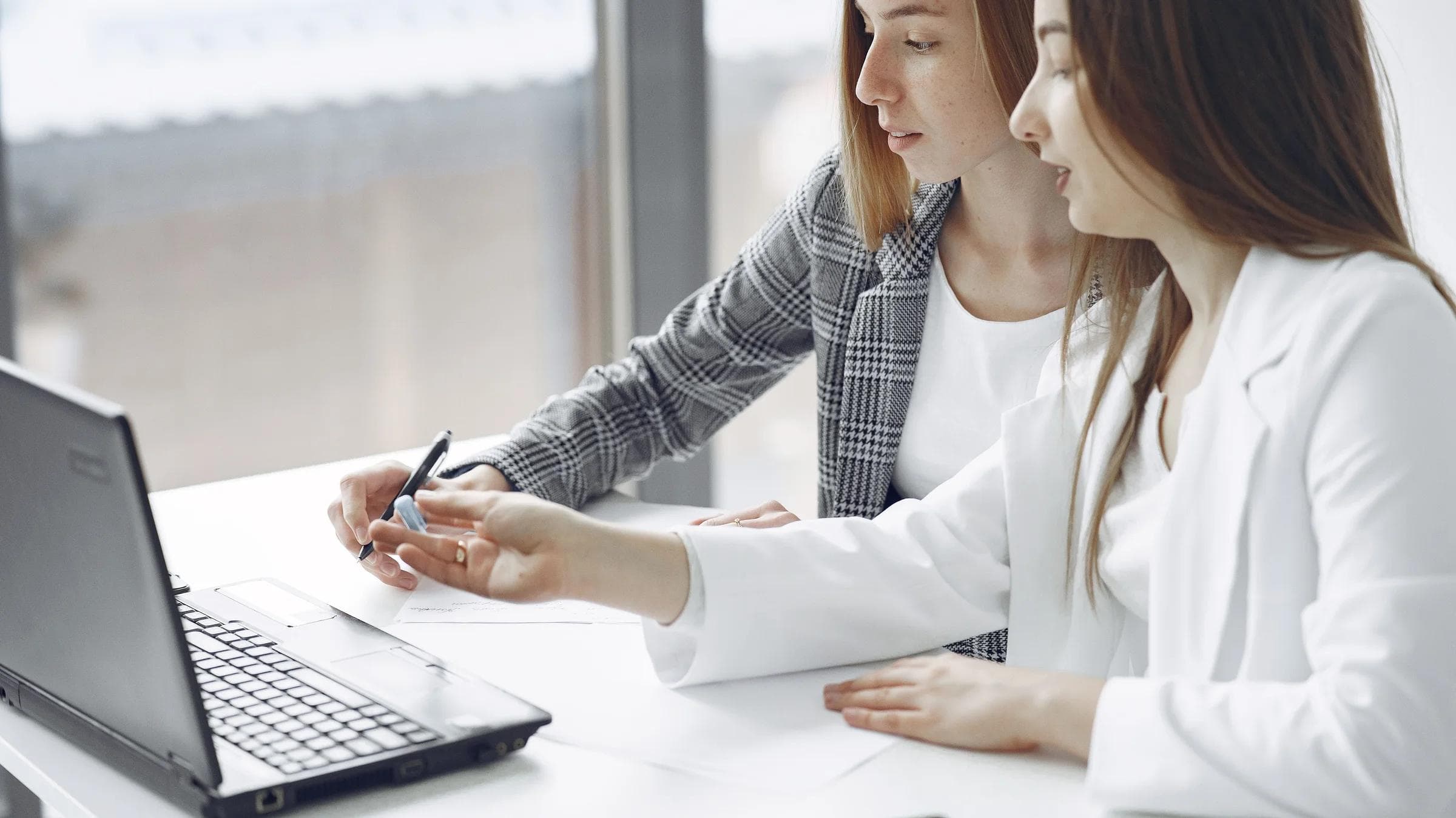 Two professional women engaged in a collaborative work session in a bright modern office.