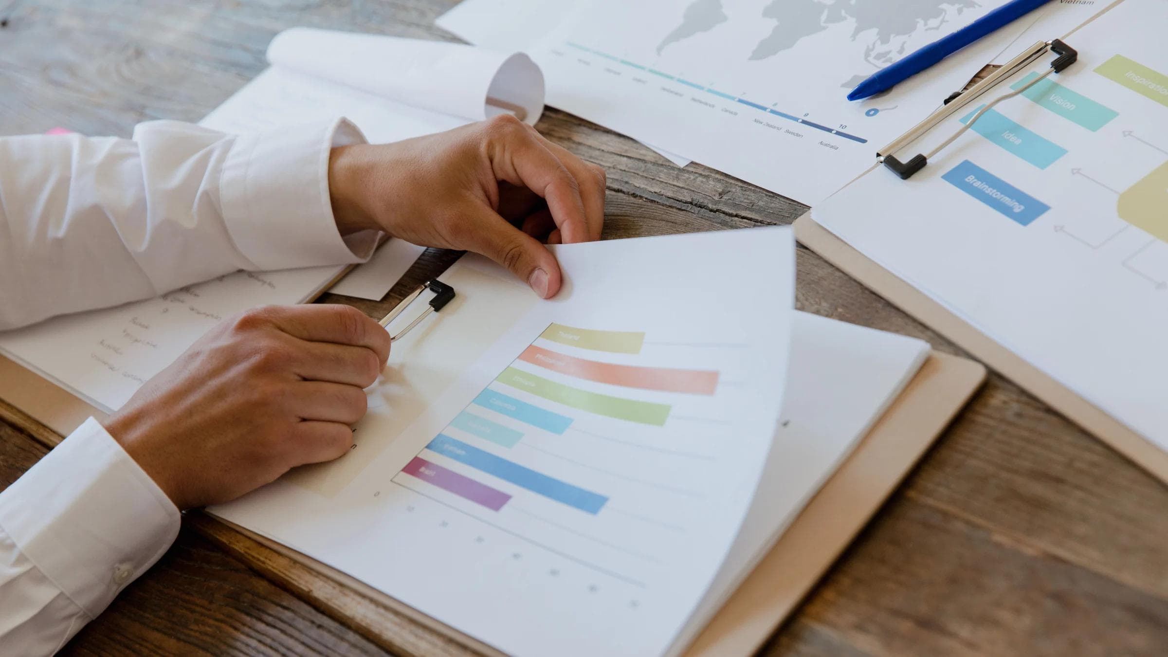 Close-up of hands reviewing business report with colorful charts and graphs on a wooden desk.