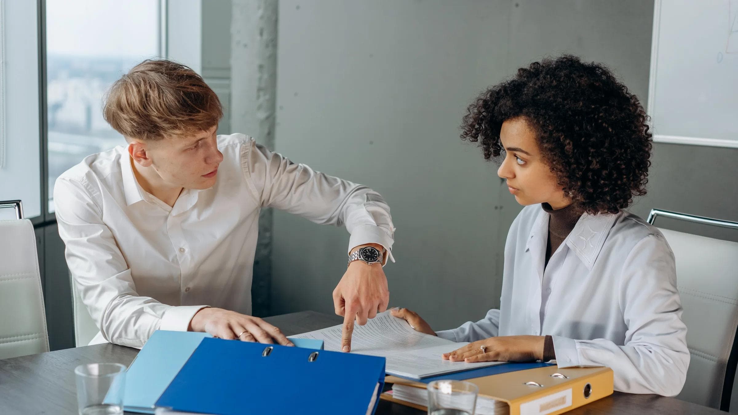 Professional workplace discussion between colleagues reviewing documents at an office table.
