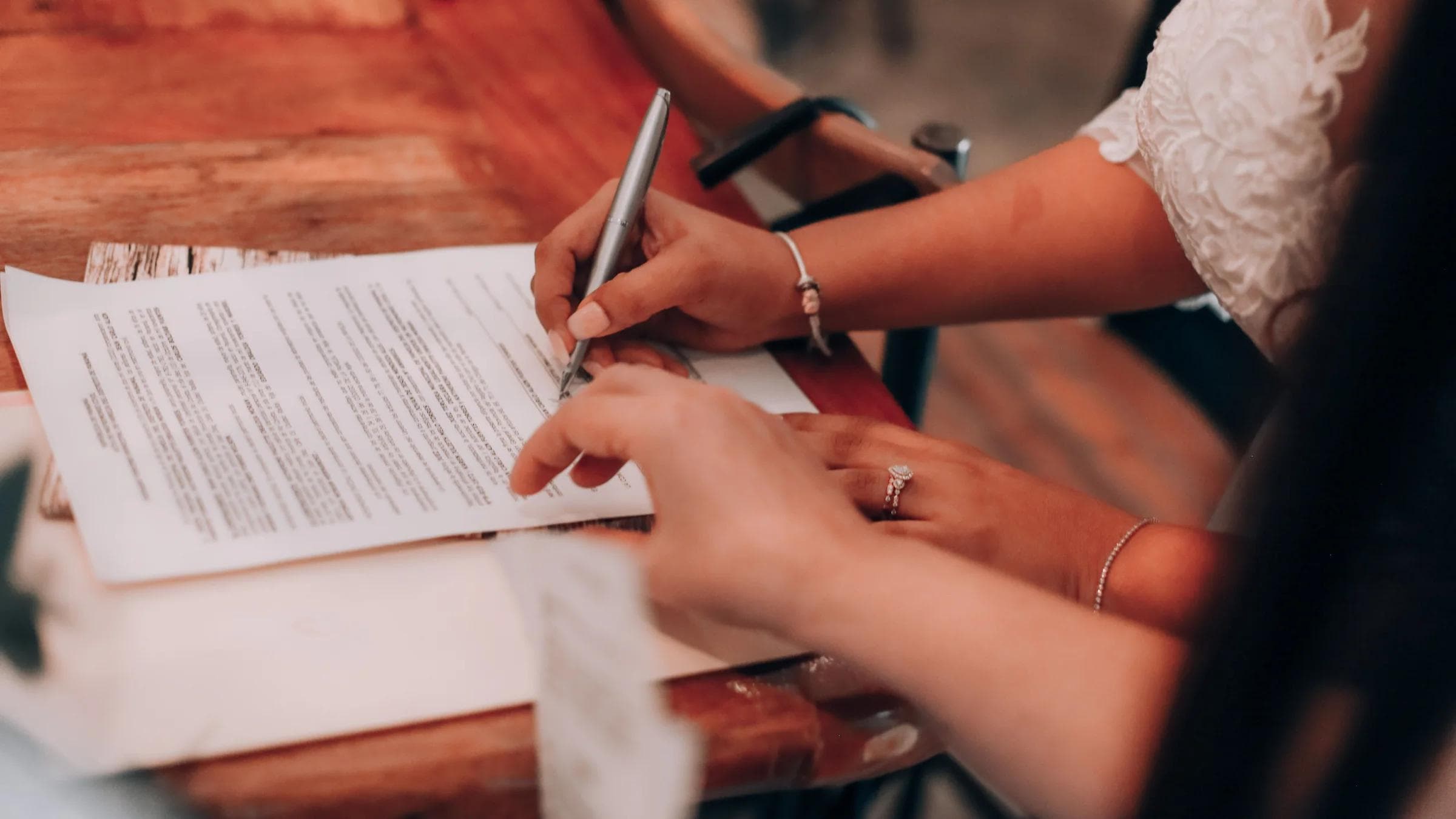 Hands signing an important document at a wooden table, symbolizing agreement and commitment.