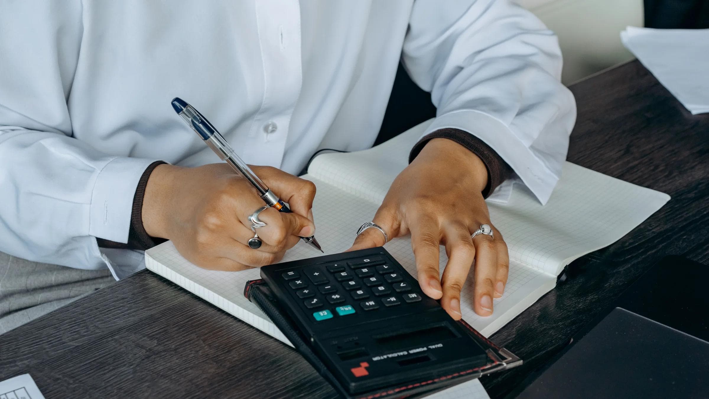 Close-up of a professional writing notes with calculator at a wooden desk.