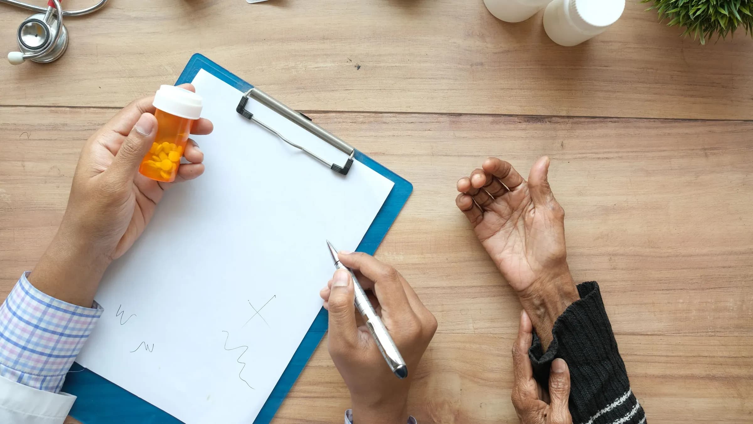 A doctor holds a pill bottle while consulting with an elderly patient. A stethoscope and prescriptions are visible.
