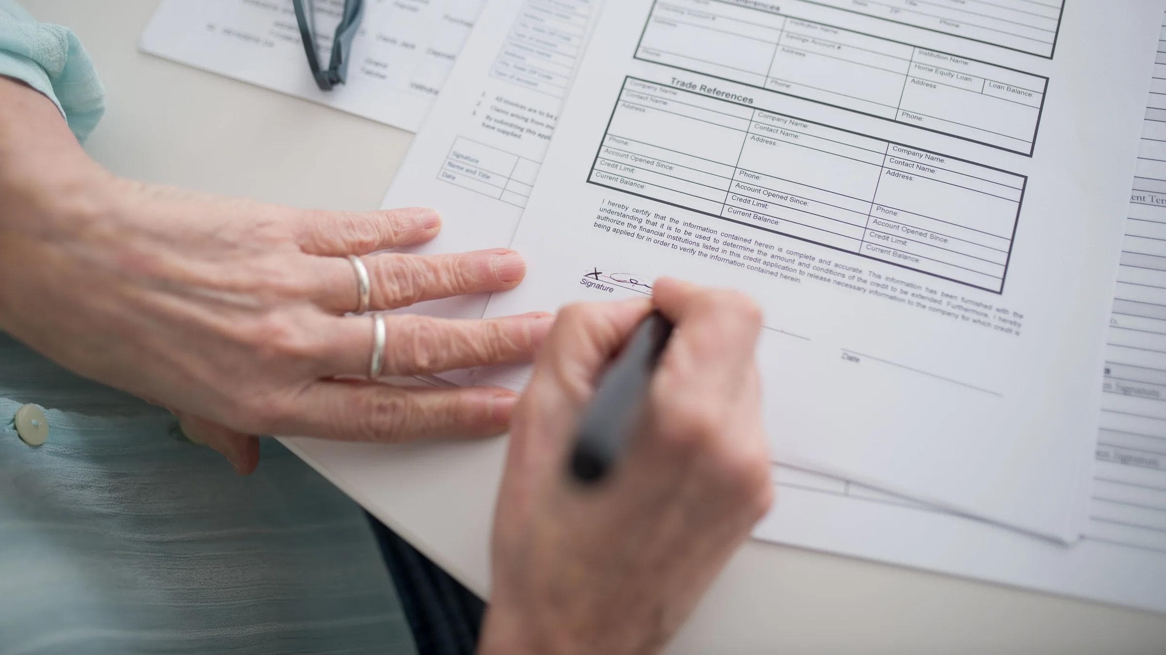 A close-up view of a hand signing official documents with a pen indoors.