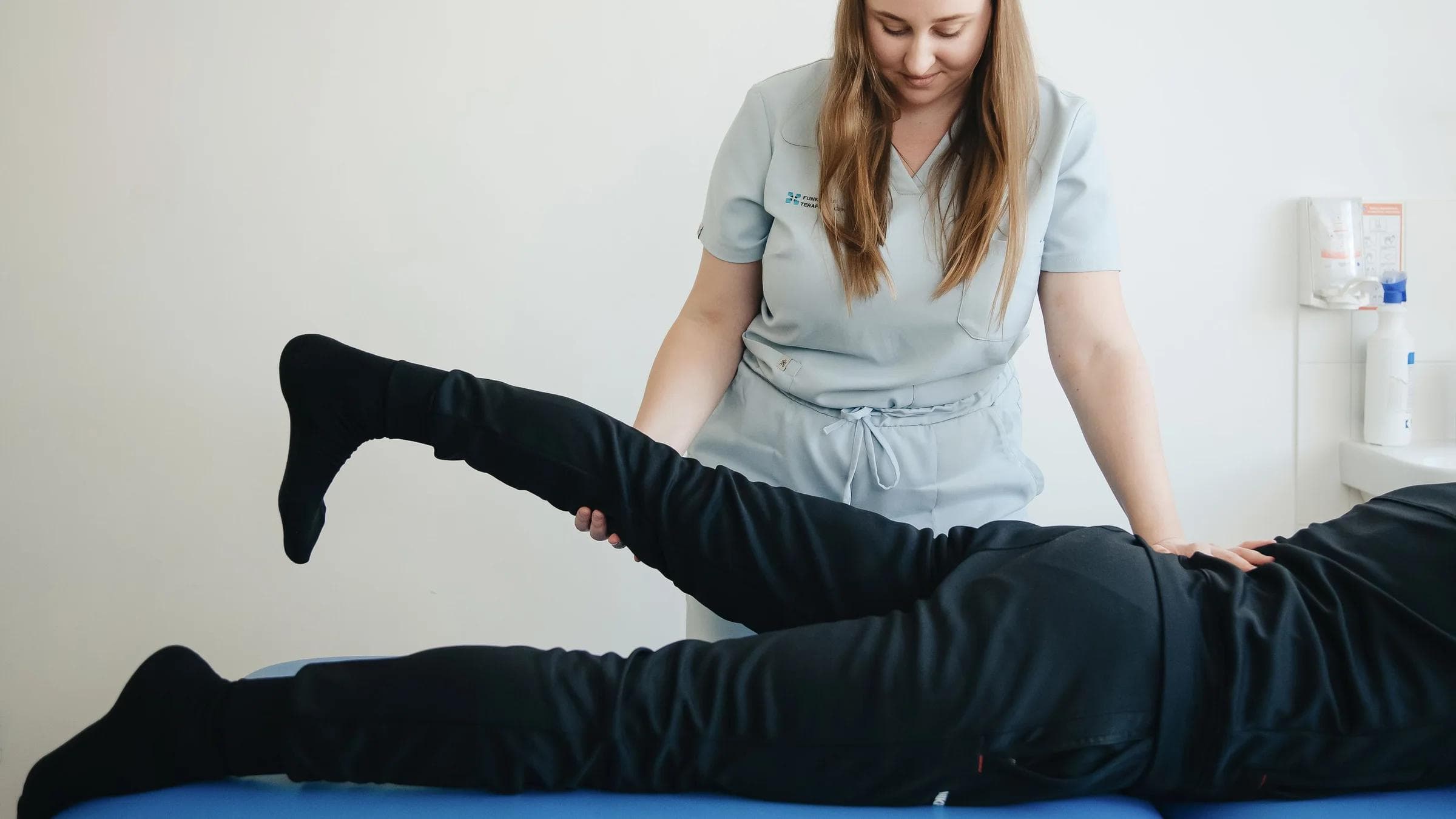 A physiotherapist helps a patient stretch their leg during a therapy session in a clinic.