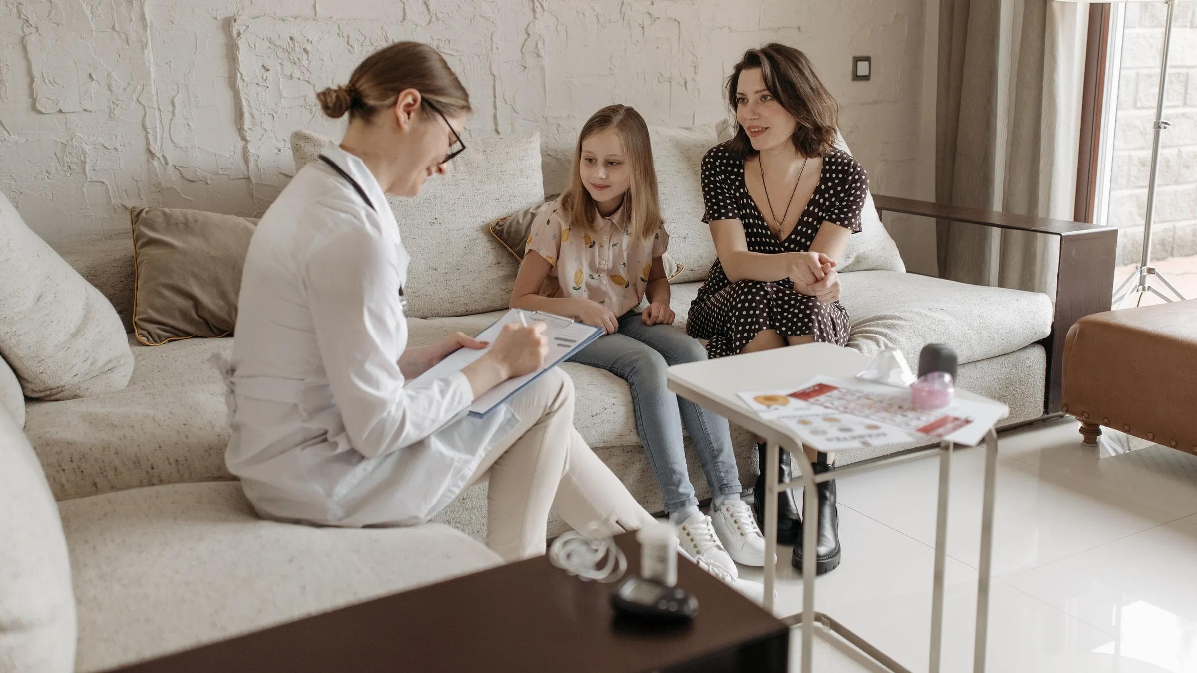 A doctor consults with a mother and daughter in a cozy indoor setting.
