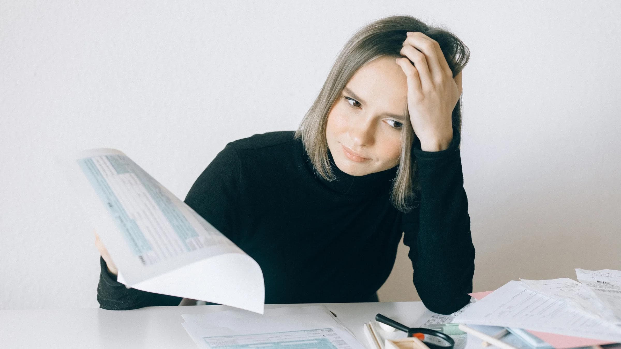 A woman showing stress while reviewing multiple paperwork and financial documents at a desk.