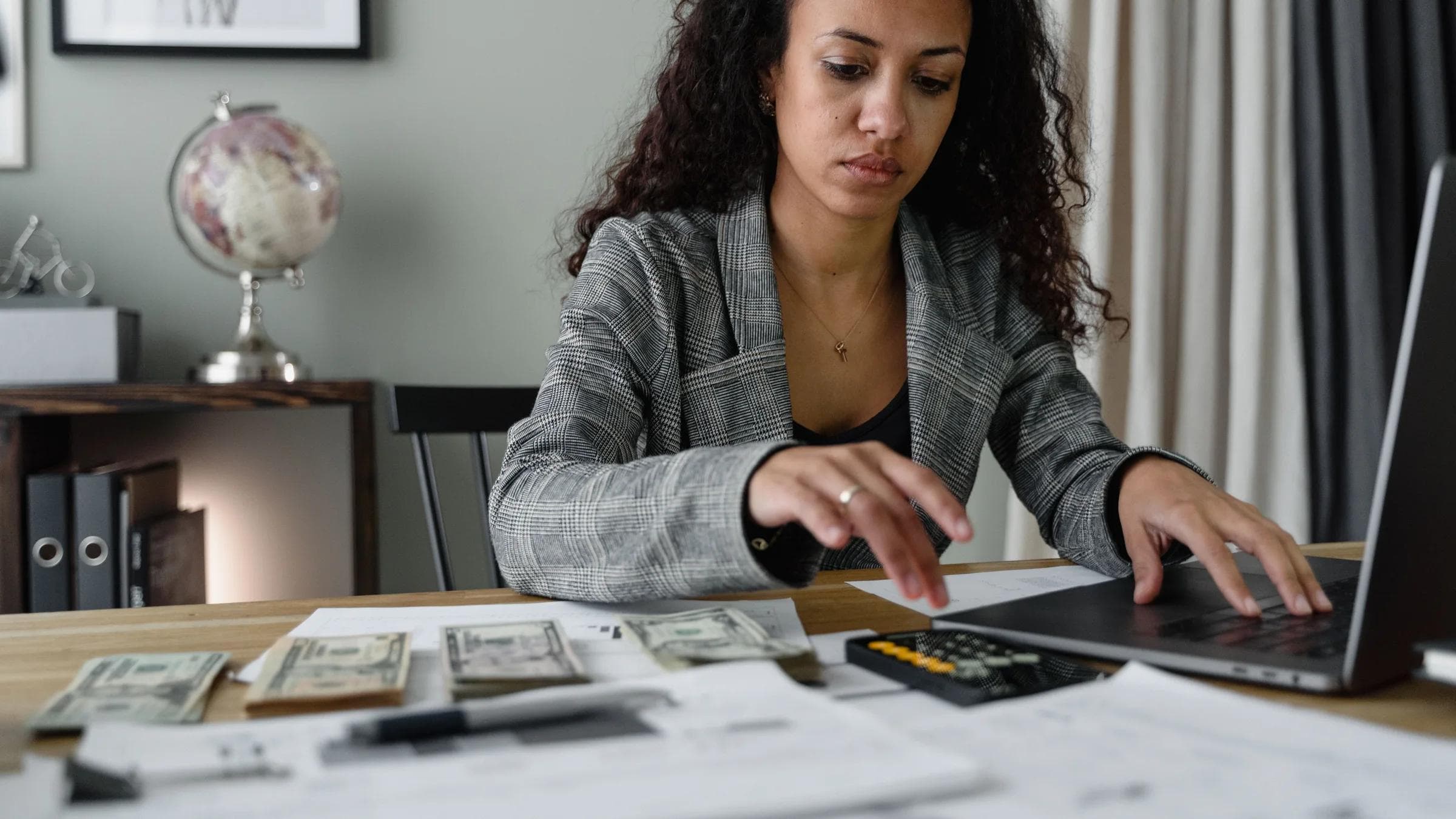 Professional woman analyzing financial documents and counting cash at office desk.