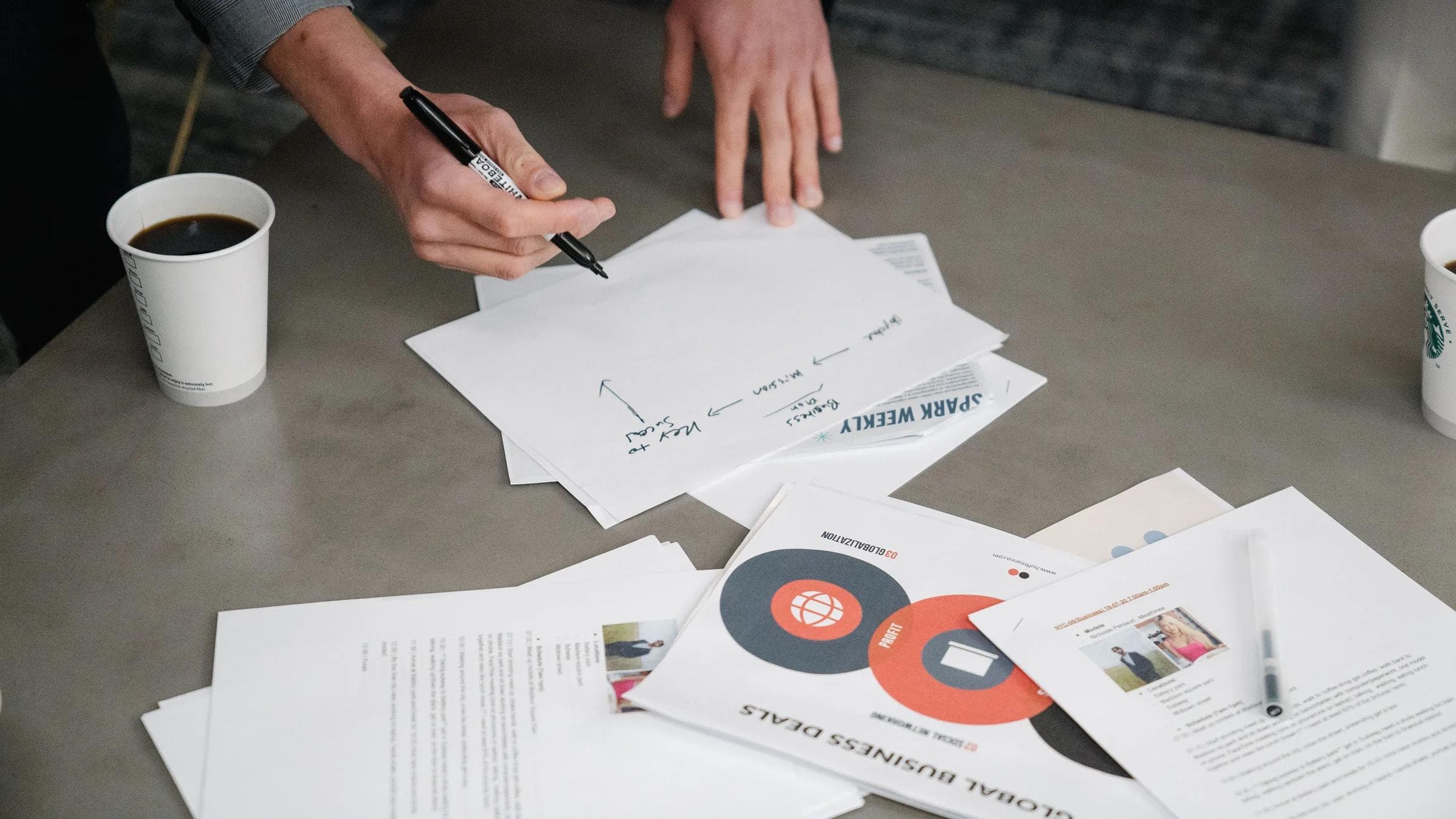Two people collaborate during a business meeting, writing notes on papers with coffee cups nearby.
