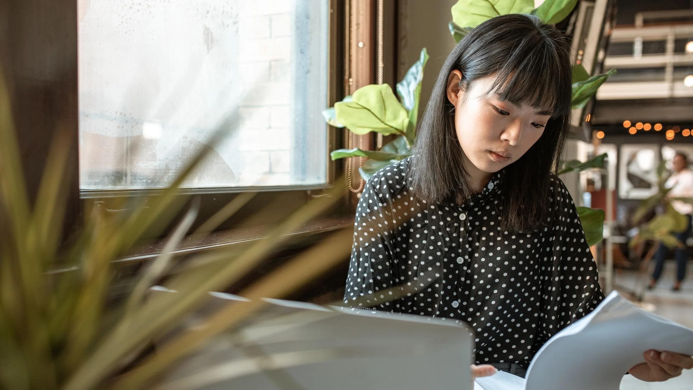 Asian woman intently working on documents at her laptop in a modern office setting.