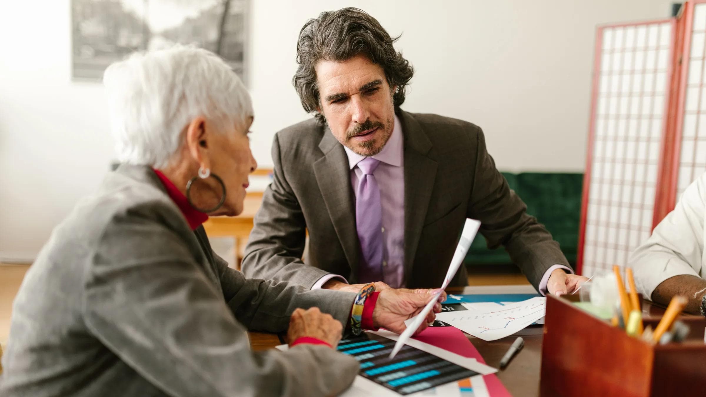 Elderly business professionals discussing reports in a modern office setting.