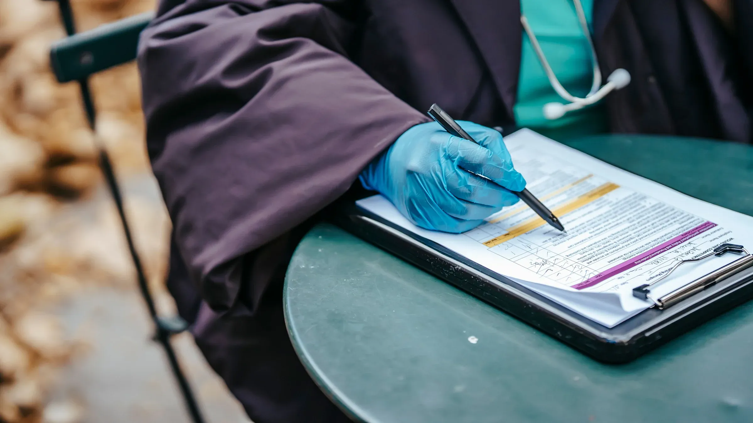 Crop anonymous female doctor in uniform with stethoscope pointing with pen at text on paper during work.