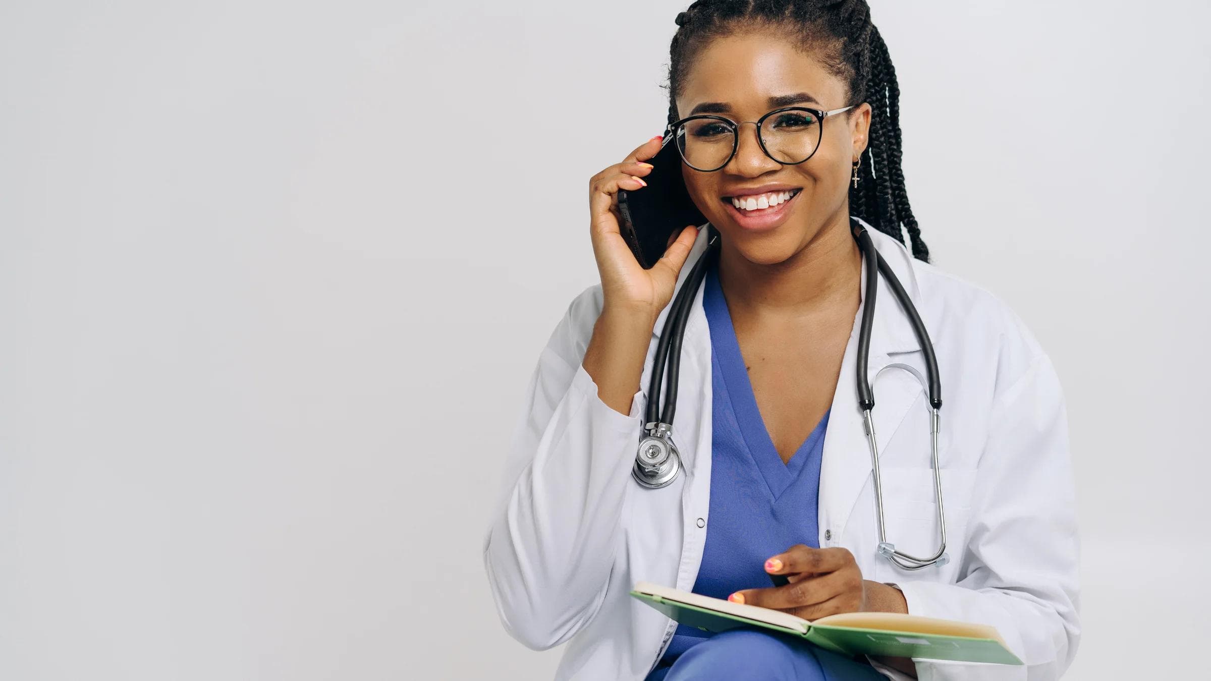 Cheerful female doctor in lab coat talking on smartphone and taking notes.