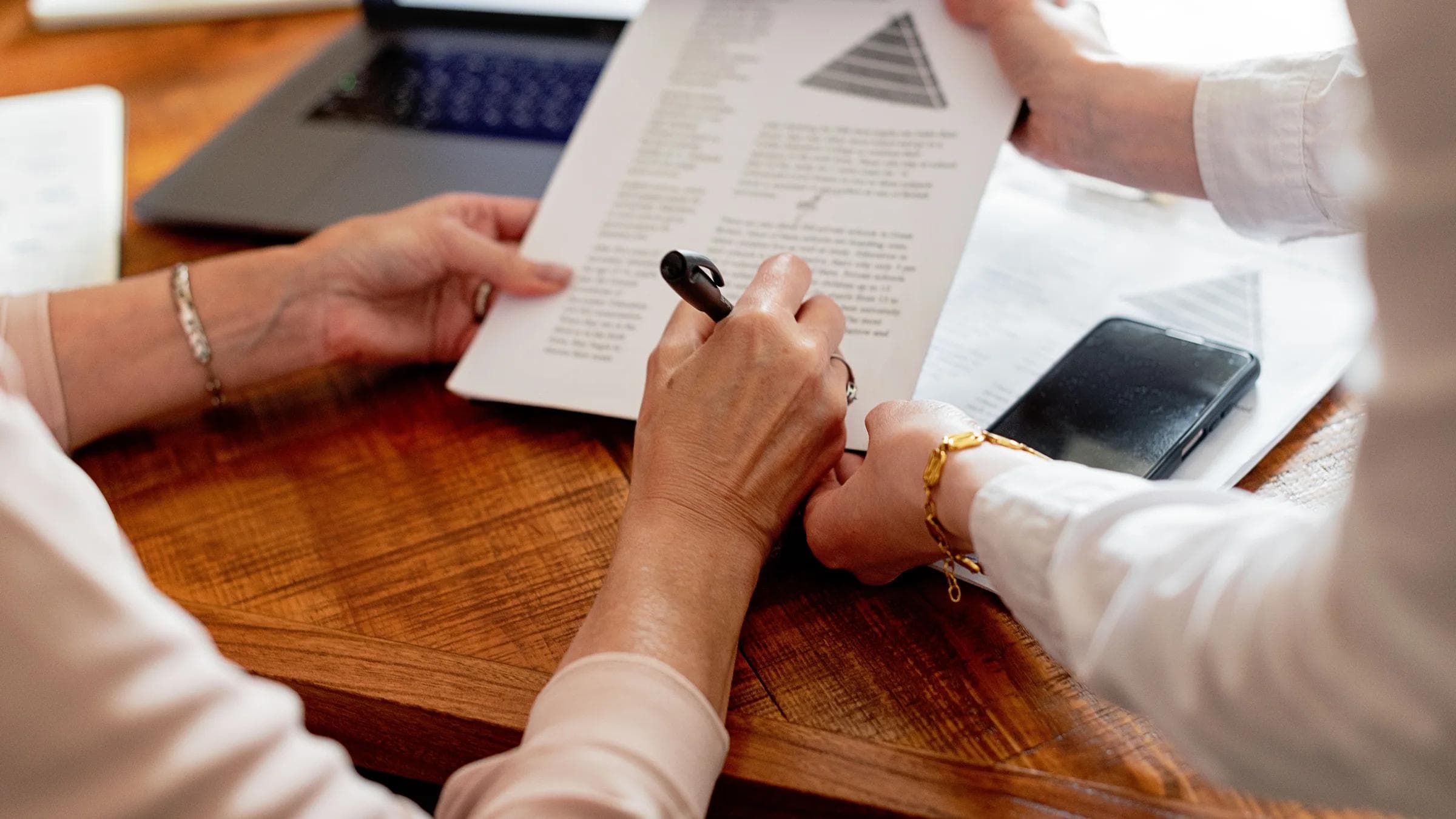 Two women reviewing documents at a table, engaging in a work discussion.