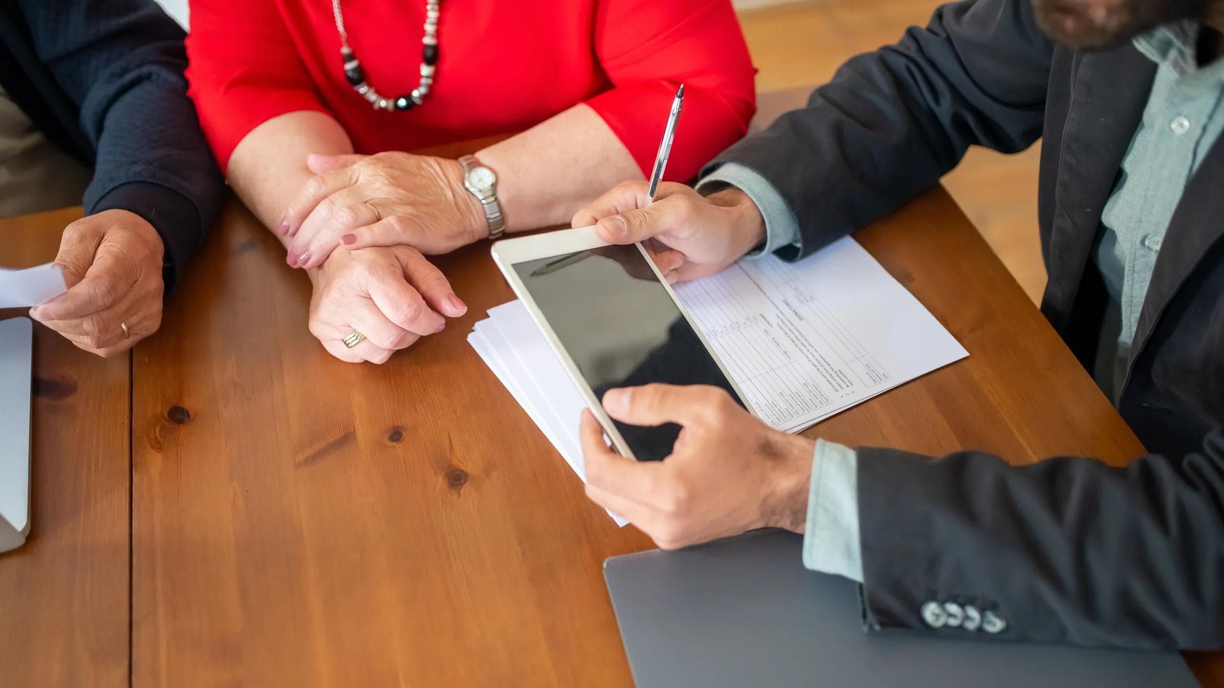 Business meeting at a wooden table with consultant reviewing documents and using a digital tablet.