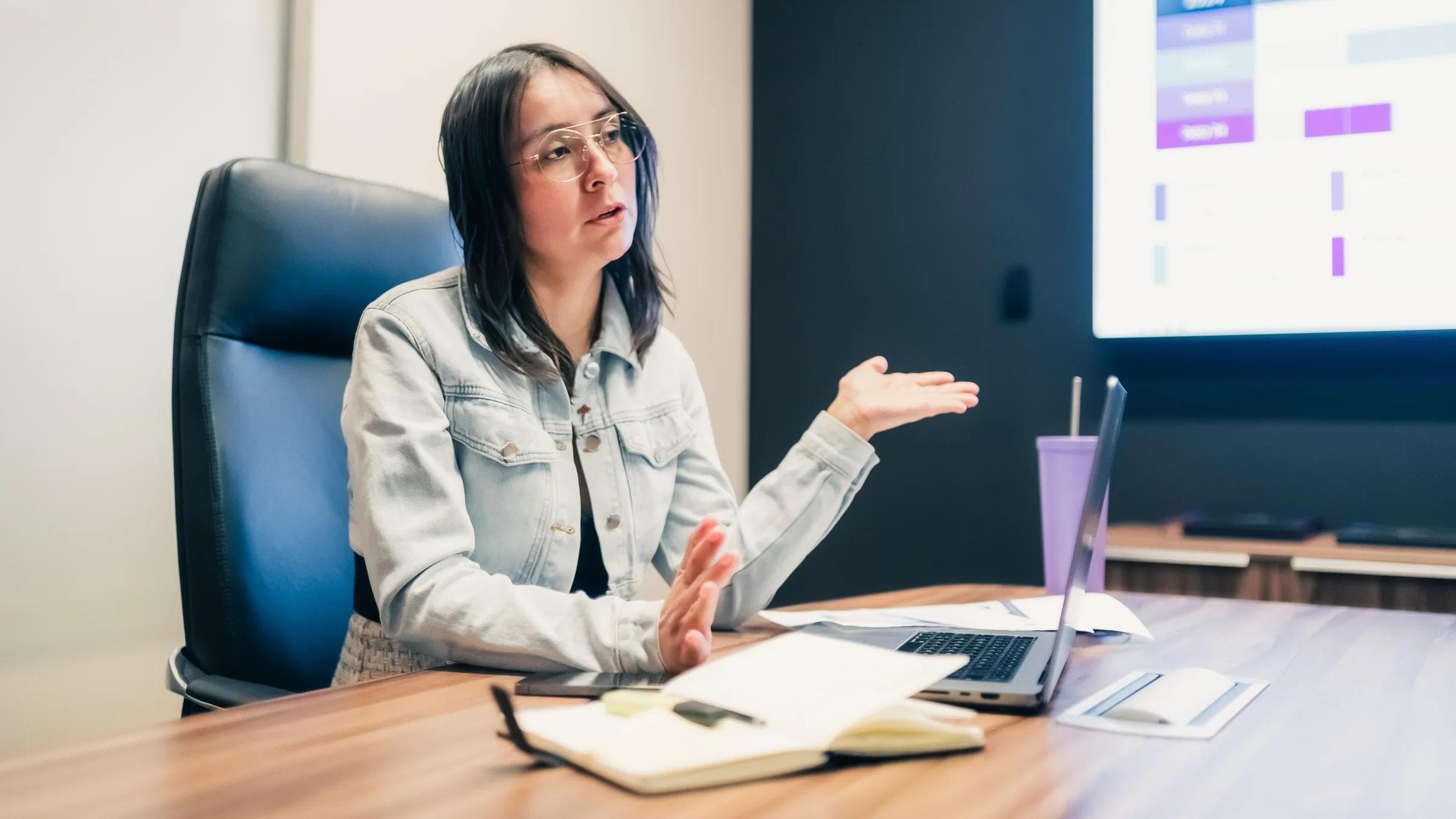 Businesswoman explaining a concept during a meeting with a presentation displayed on screen.