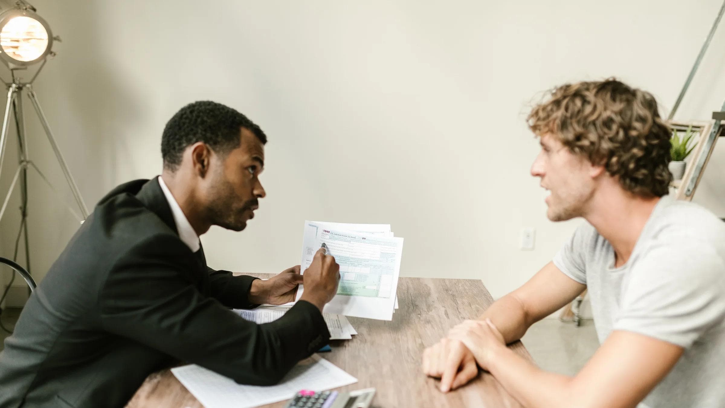 A financial advisor discusses paperwork with a client at a desk in a modern office.