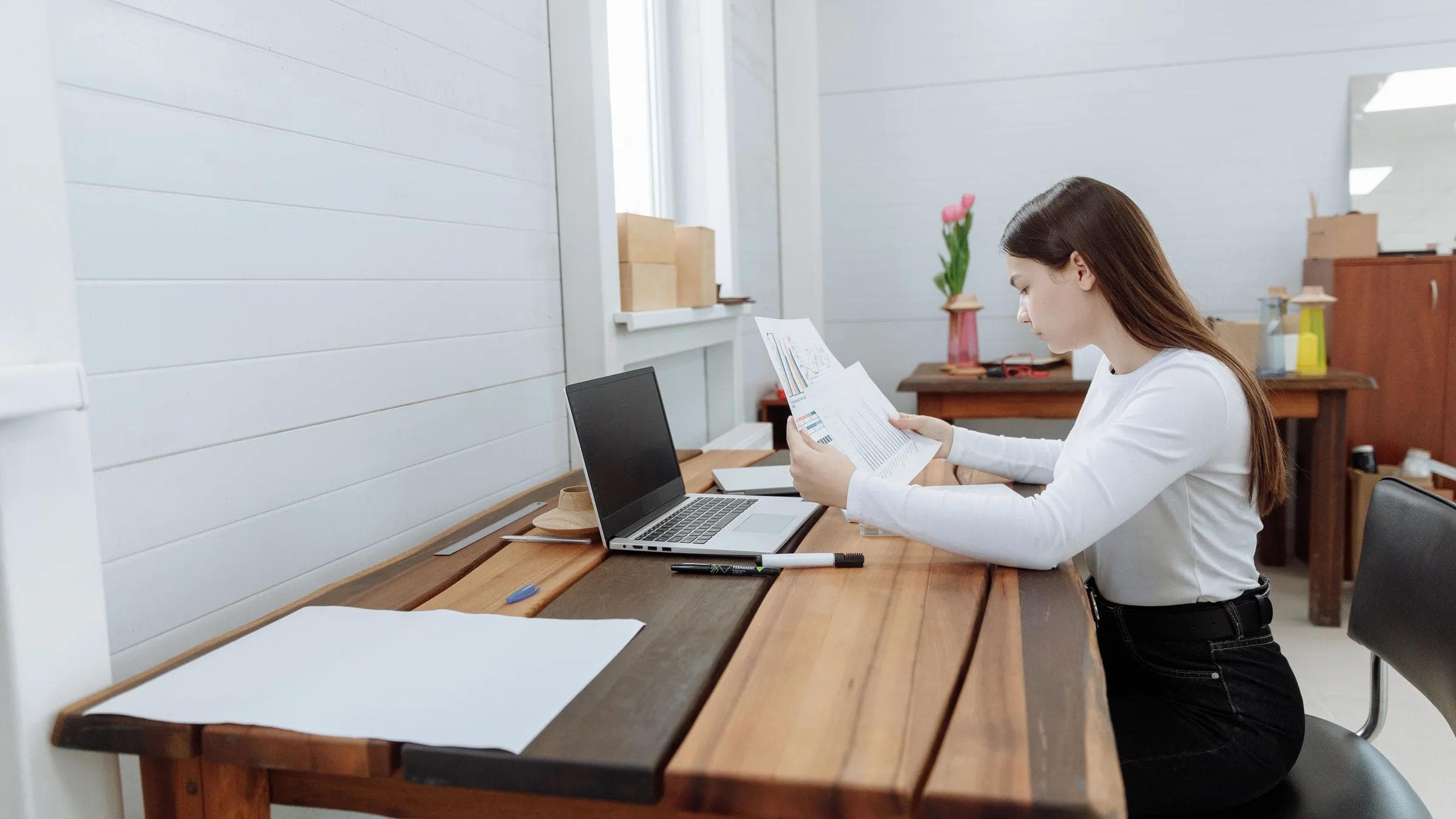 Focused woman working remotely on a laptop at a wooden desk in a home office setting.