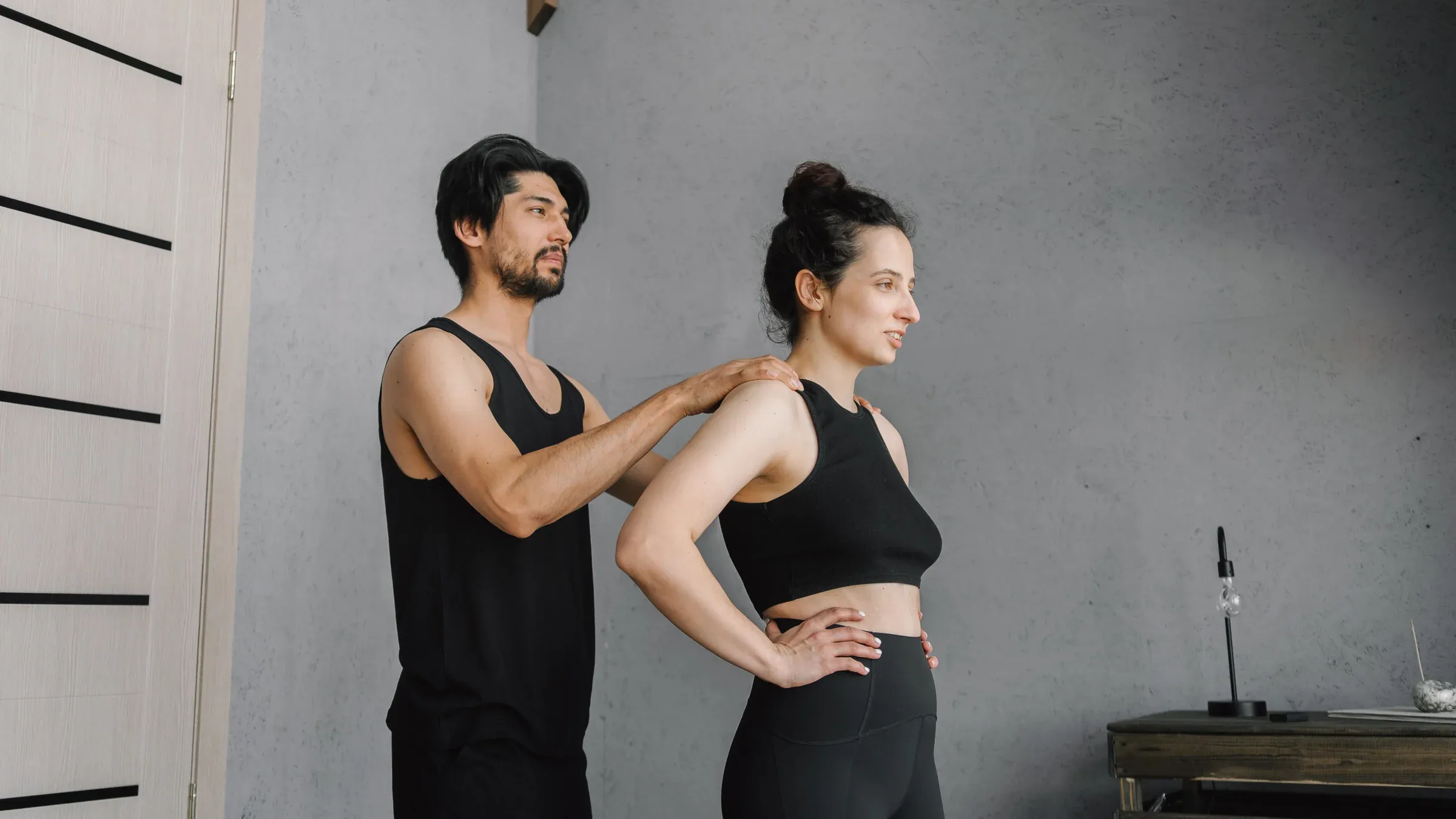 Fitness coach assisting woman with stretching exercises indoors.