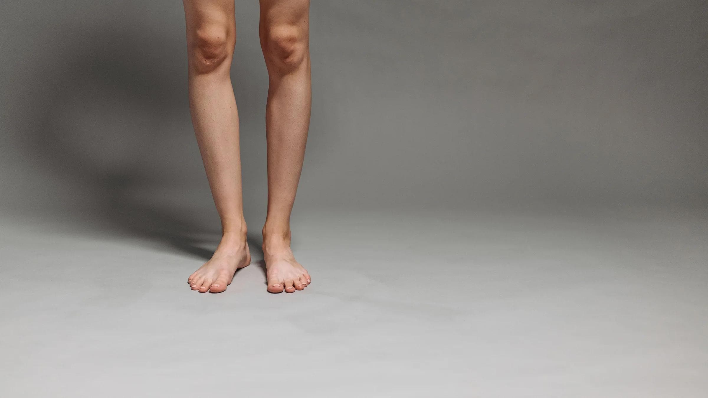 Studio shot of a person's lower legs and feet on a gray background.