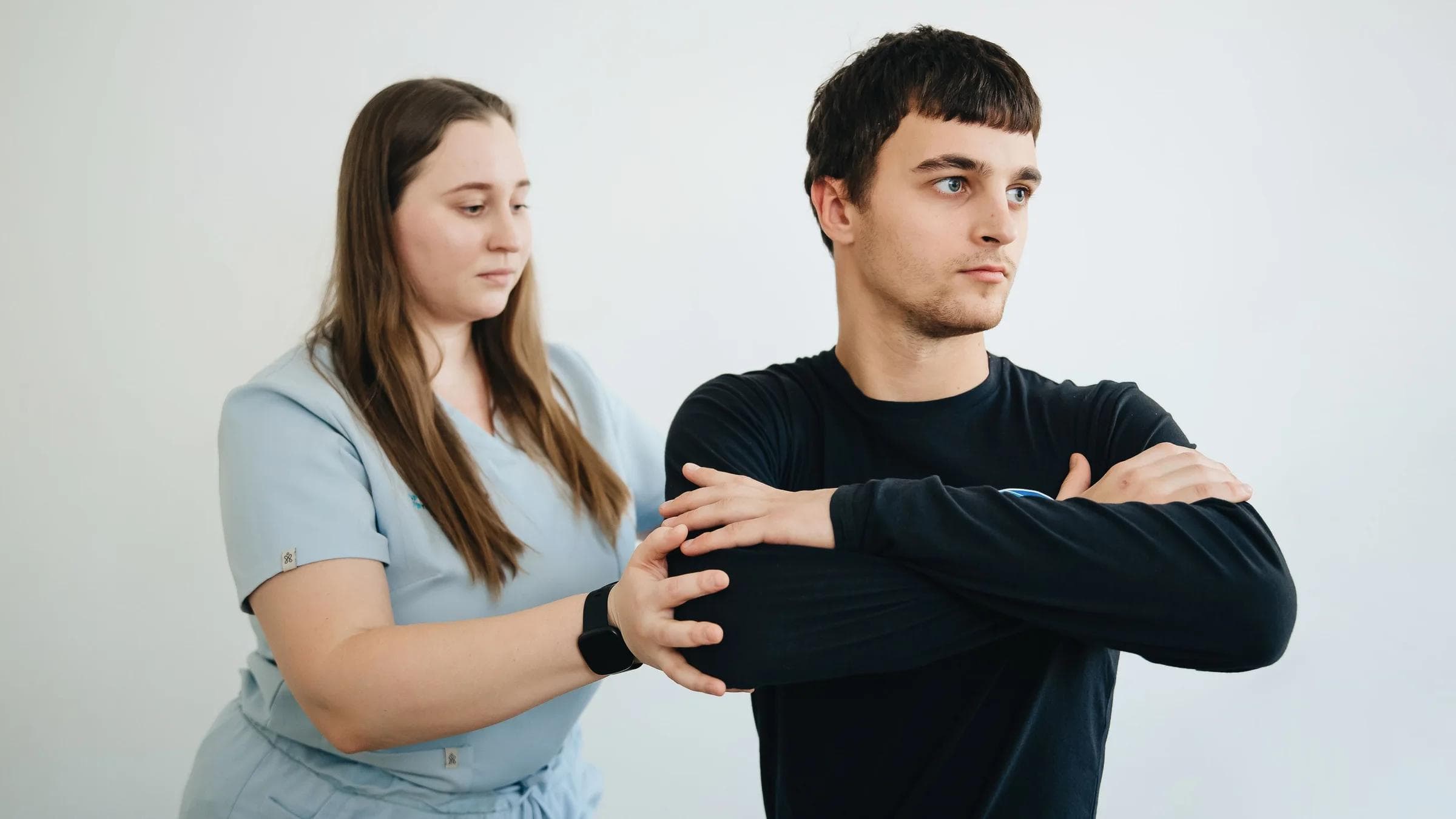 A physiotherapist assists a person in arm exercises in a clinical setting.