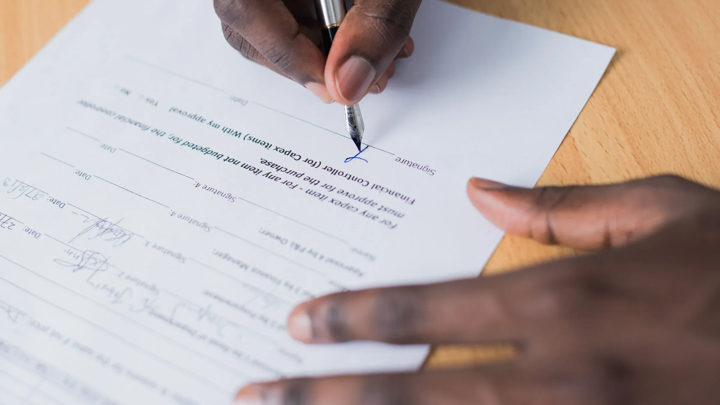 A close-up view of a person's hand signing a business contract on a desk with a pen.