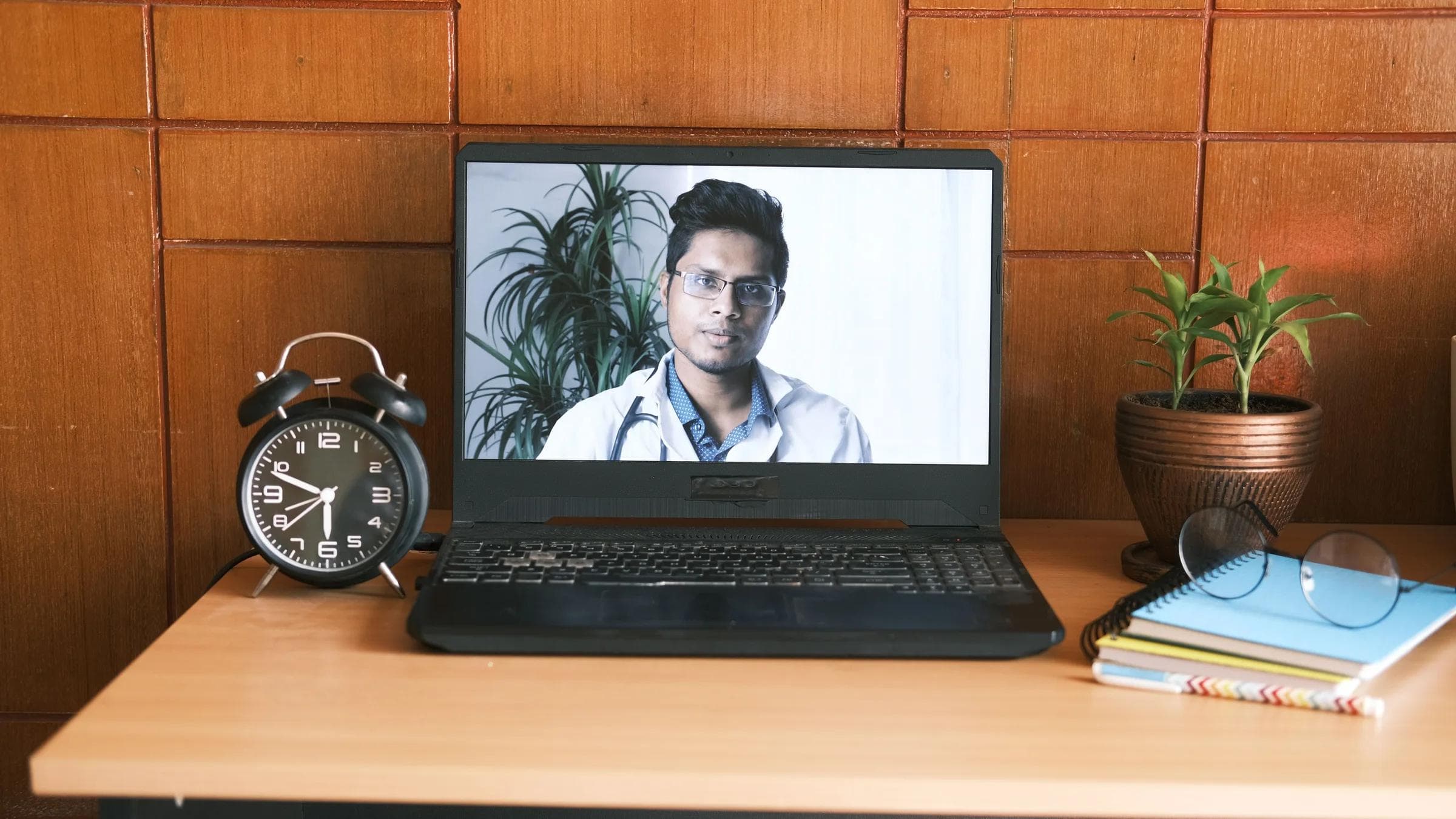 A home office desk with a laptop showing a virtual doctor, ideal for online consultation themes.