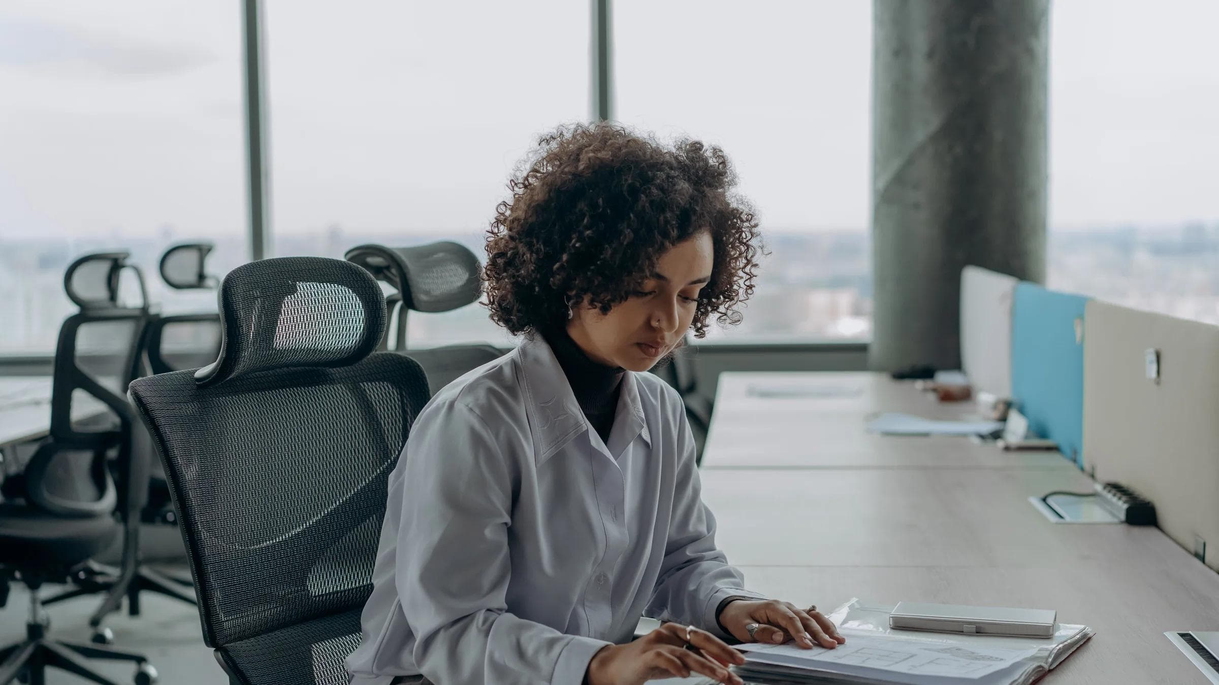 A professional woman with curly hair calculating documents in a modern office setting.