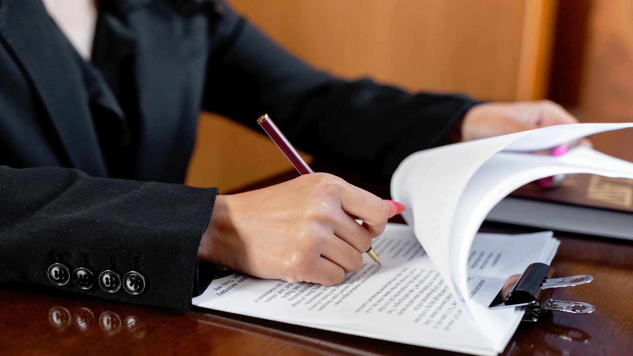 Close-up of a woman signing legal documents with a pen in an office setting.