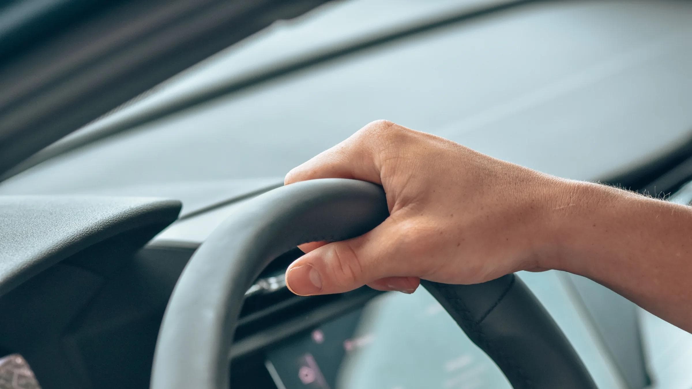 A close-up shot of a hand gripping a steering wheel in a modern car interior.