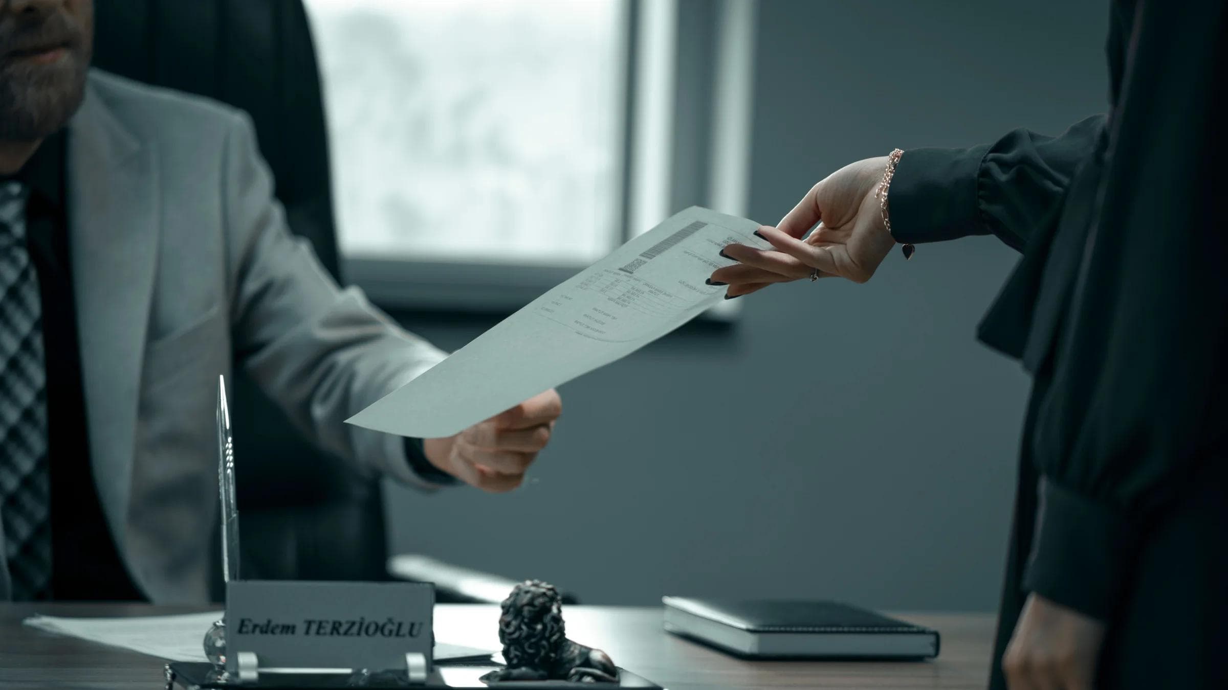 A formal business interaction with document exchange between professionals in a modern office setting.
