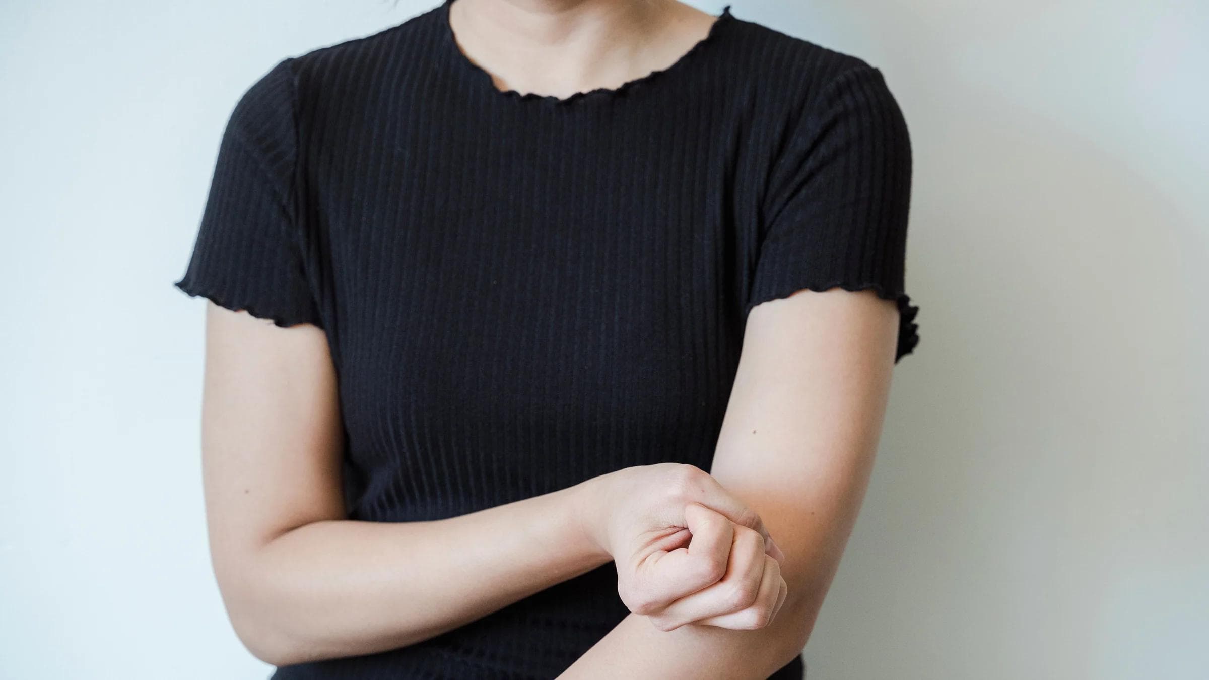 A close-up view of a woman in a black shirt holding her arm, showcasing skin contact and emotion.