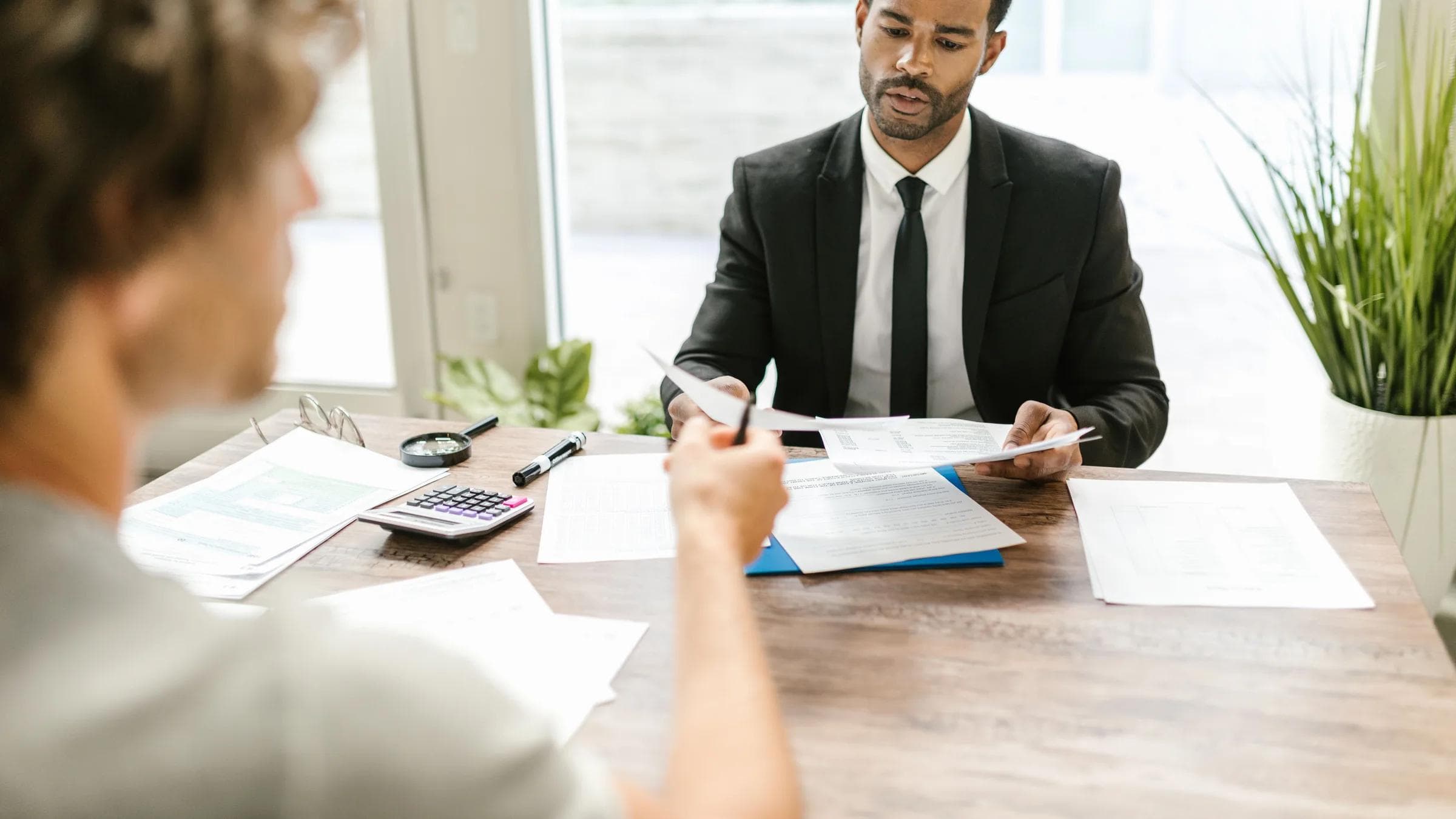 Businessman in a suit reviewing documents during a meeting indoors with a colleague.