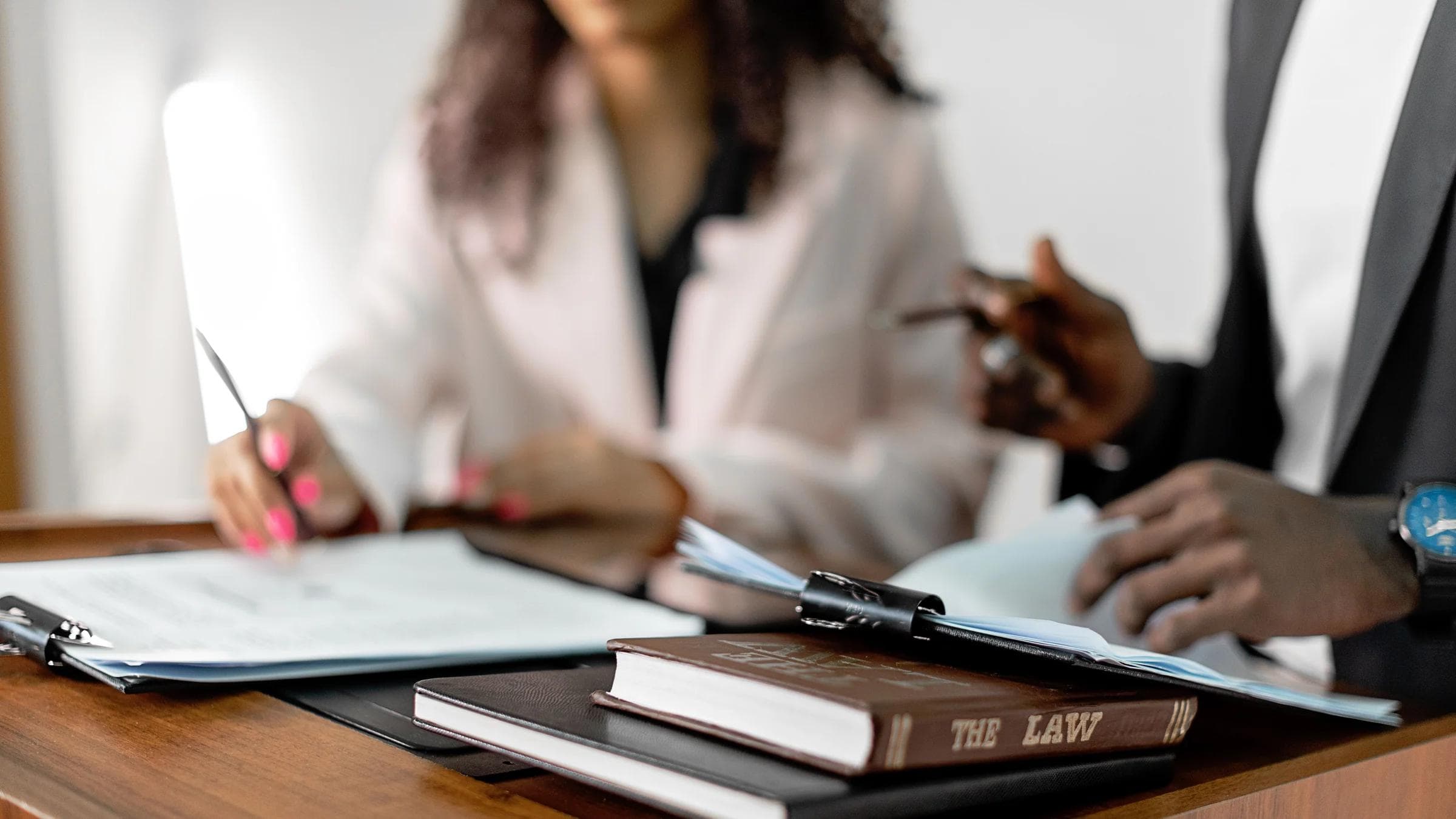 Two lawyers reviewing documents with law books on a desk. Professional legal environment.