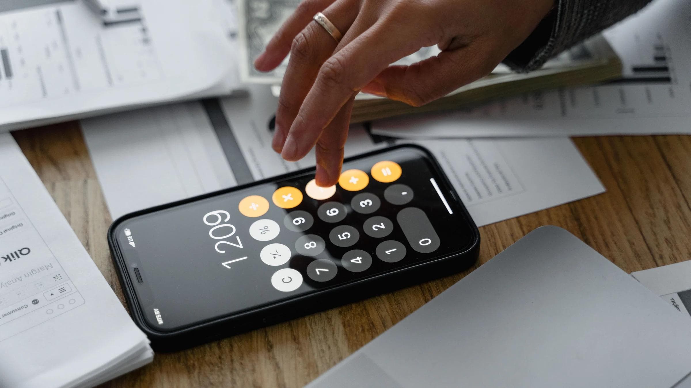 Close-up of a person using a smartphone calculator on a table with documents for financial calculations.