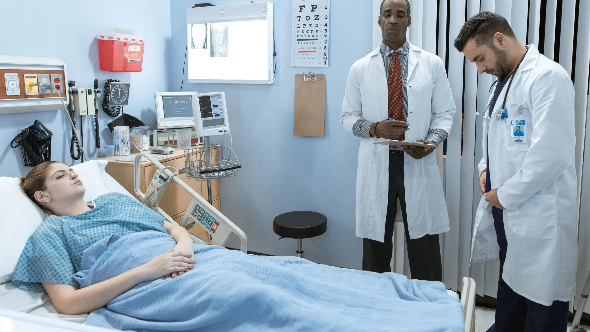 Doctors in lab coats attend to a patient lying in a hospital bed, emphasizing healthcare and medical care.