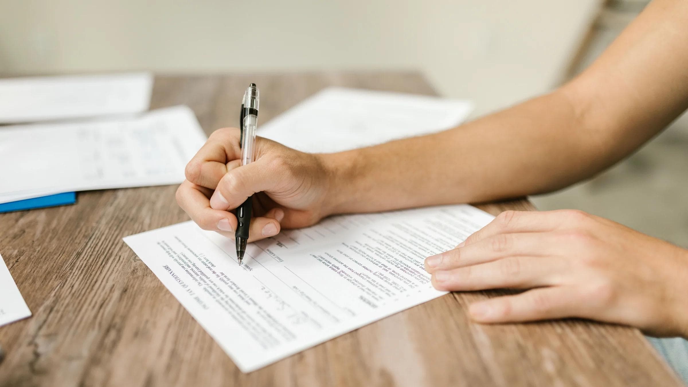 Hand filling out paperwork with a pen, showcasing focus on document completion.