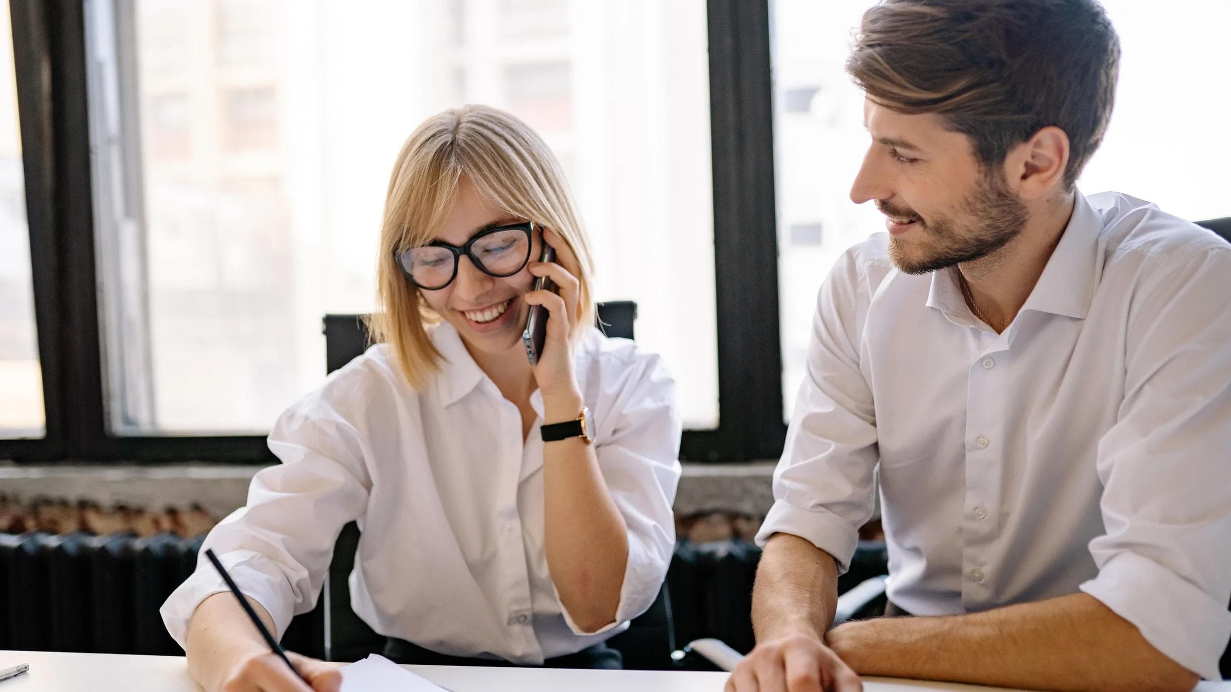 Two colleagues collaborate in a bright office, sharing ideas and notes.